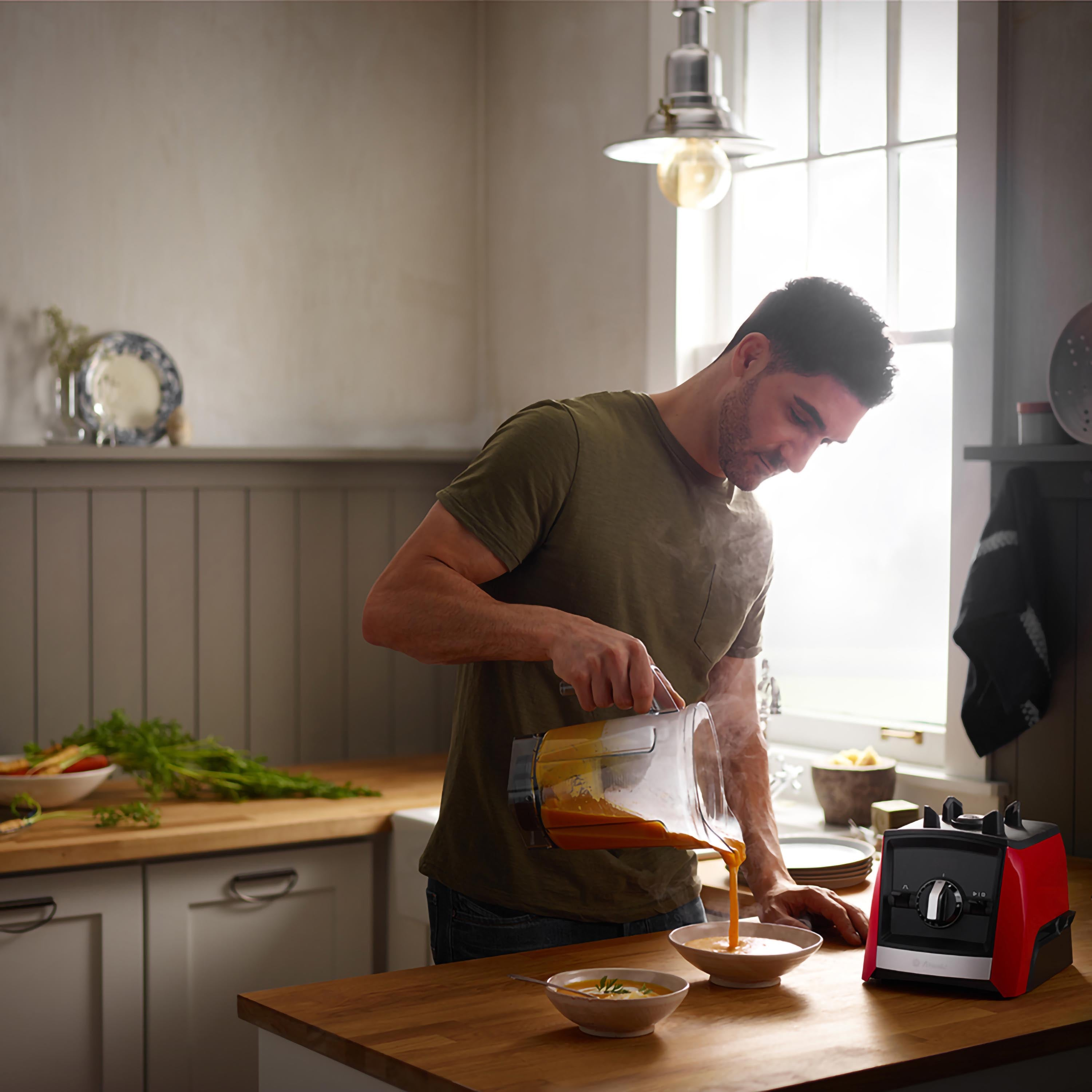 Uomo che versa zuppa da un frullatore in ciotole in una cucina. Un frullatore rosso è sul bancone.