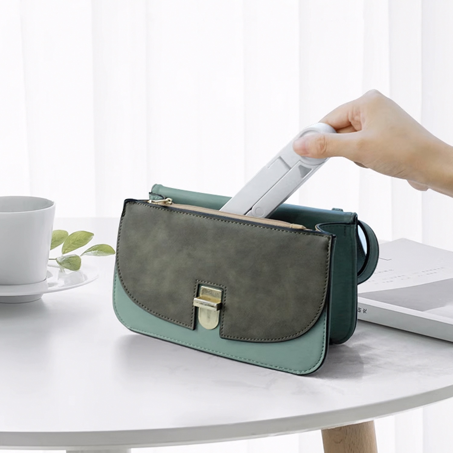 Eine Hand steckt einen kleinen, weißen Faltfächer in eine grün-blaue Handtasche.