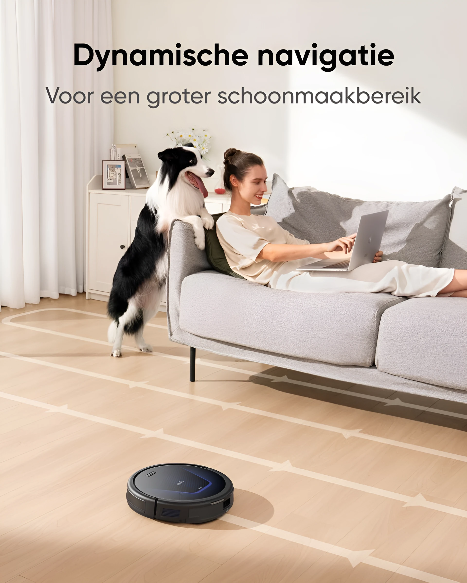 Eine Frau benutzt einen Laptop, ein Hund und ein Roboter-Staubsauger auf dem Boden.