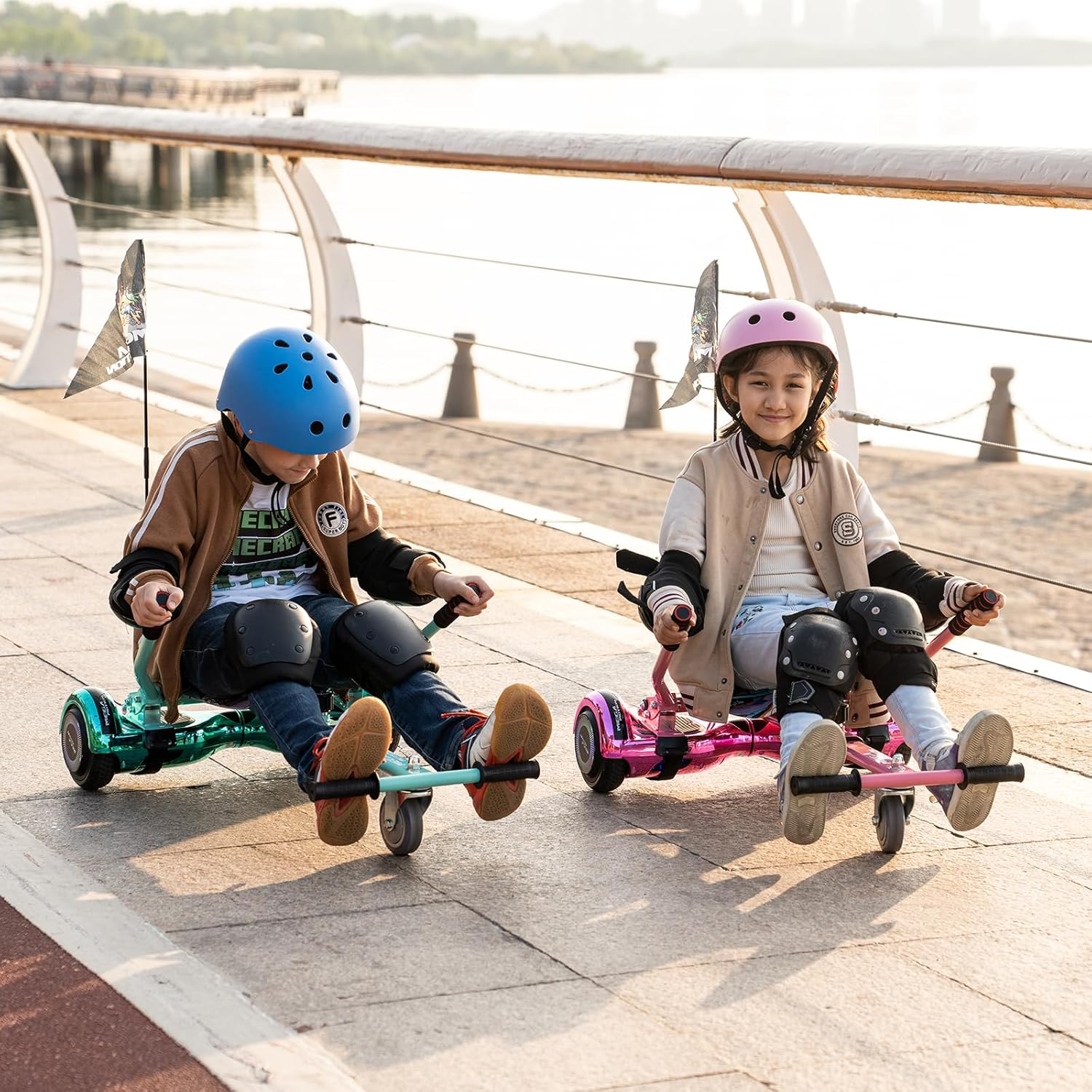 Dwoje dzieci jeżdżących na deskorolkach elektrycznych. Mają na sobie kaski i ochraniacze na kolana. Otoczenie jest słoneczne.