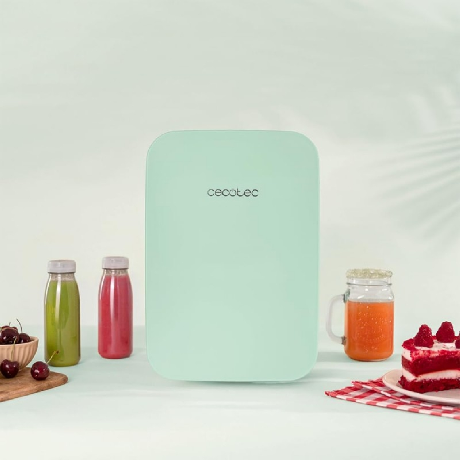 Una pequeña nevera verde menta con jugos y pastel en una mesa, con cerezas.