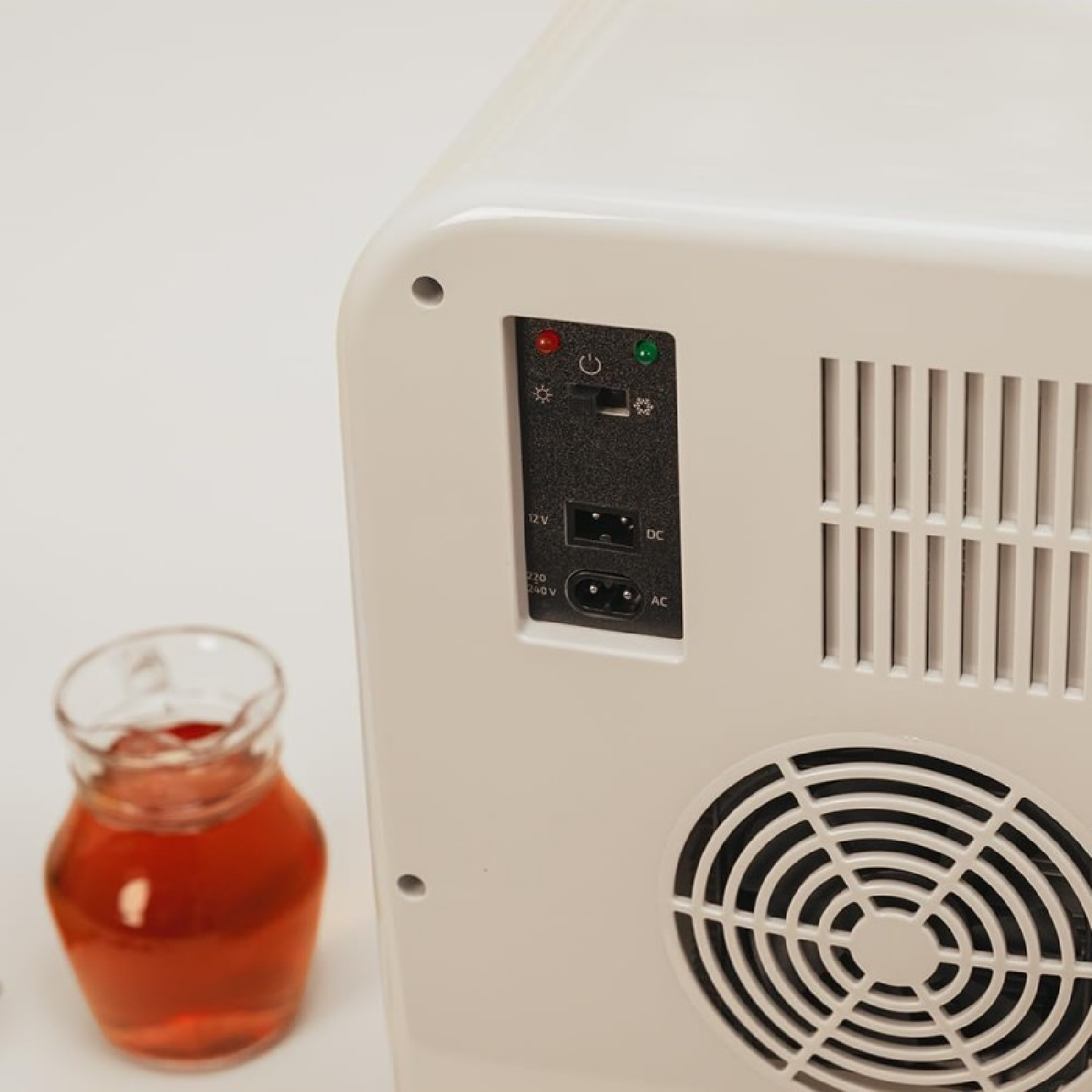 Primo piano di un mini frigo bianco con pulsanti di accensione e controllo. Brocca di vetro a sinistra.