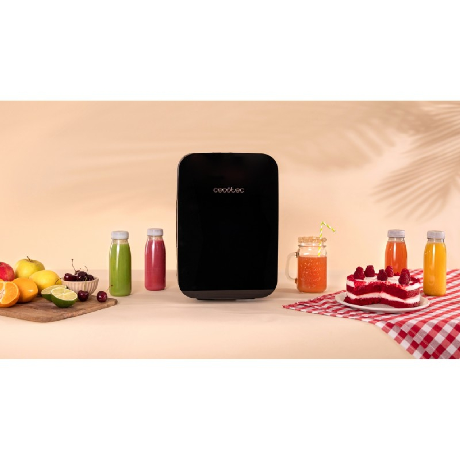 Un refrigerador portátil negro está rodeado de botellas de jugo, frutas y pastel.