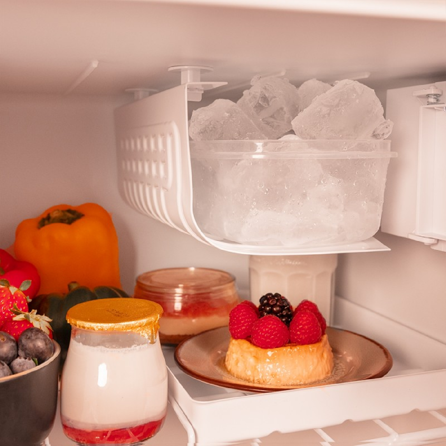 Wnętrze lodówki z lodem, owocami i deserem. Żółta papryka, truskawki i ciasto z jagodami.