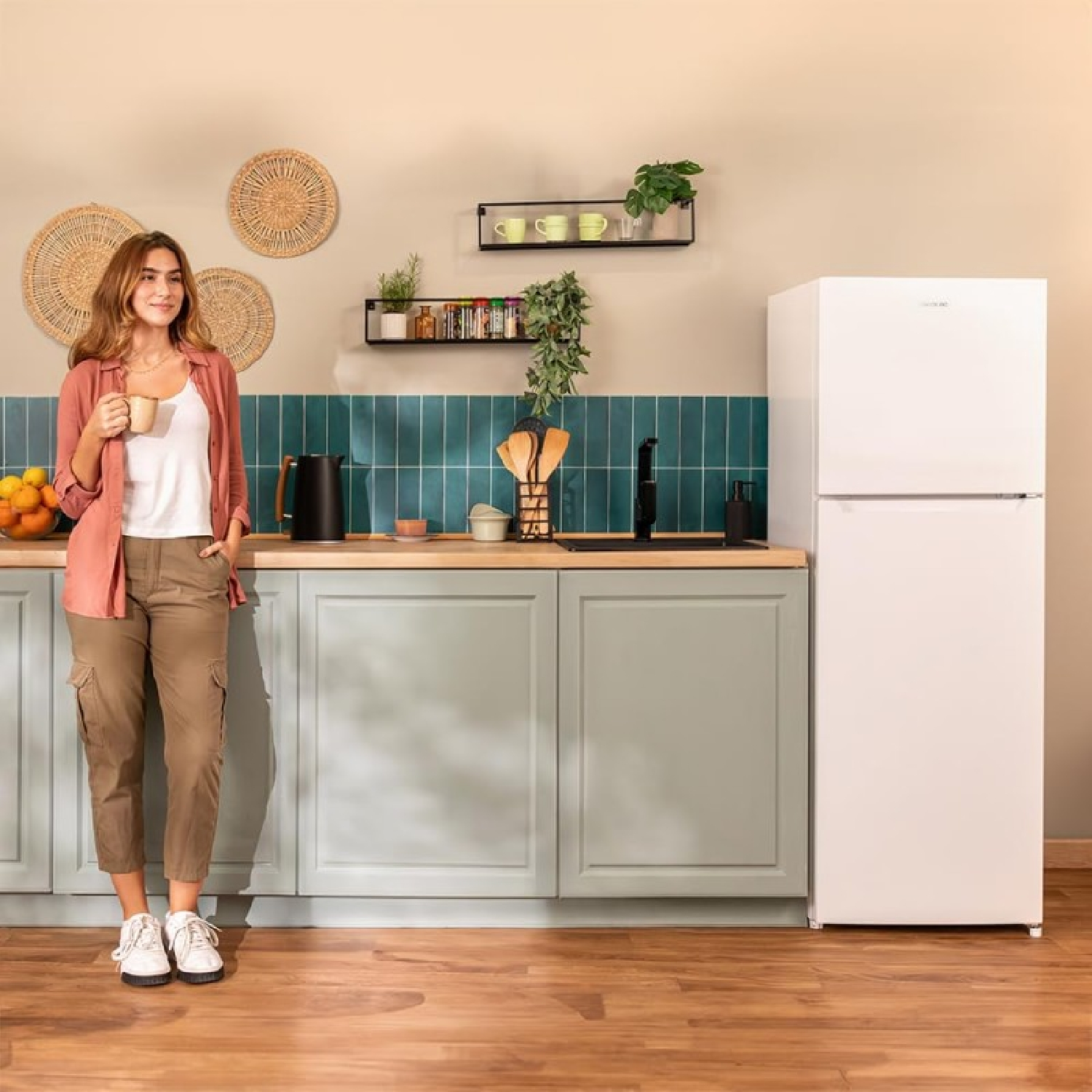 Donna vicino al frigorifero, che tiene una tazza. Ambiente cucina con pavimento in legno e piastrelle blu.