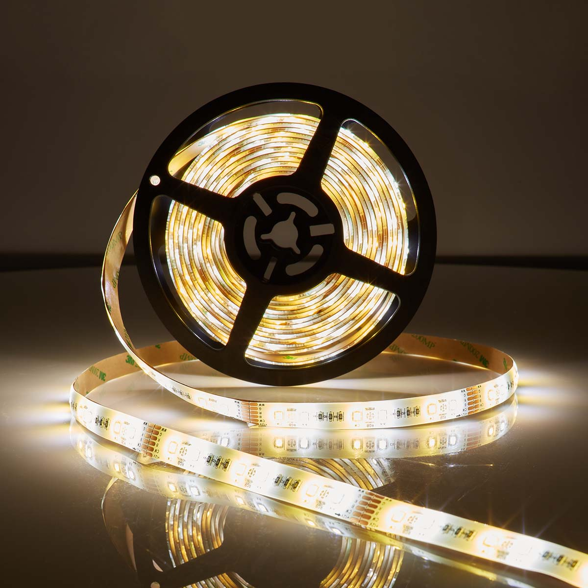 LED light strip rolled on a black spool. The strip emits white light. The background is dark.