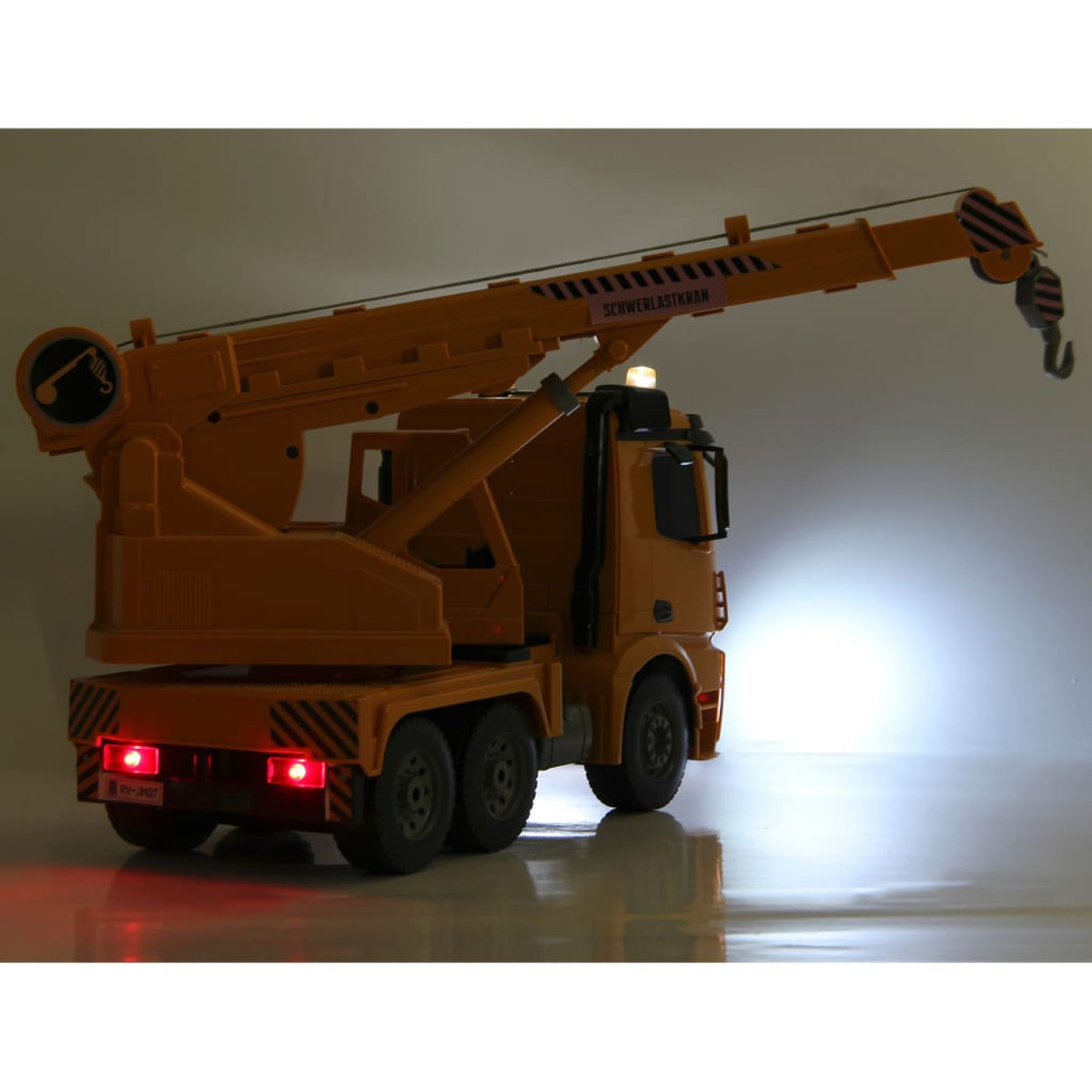 Pomarańczowa zabawka dźwig ciężarowy z wysięgnikiem. Czerwone światła są włączone. Widoczne słowo Schwerlastkran.