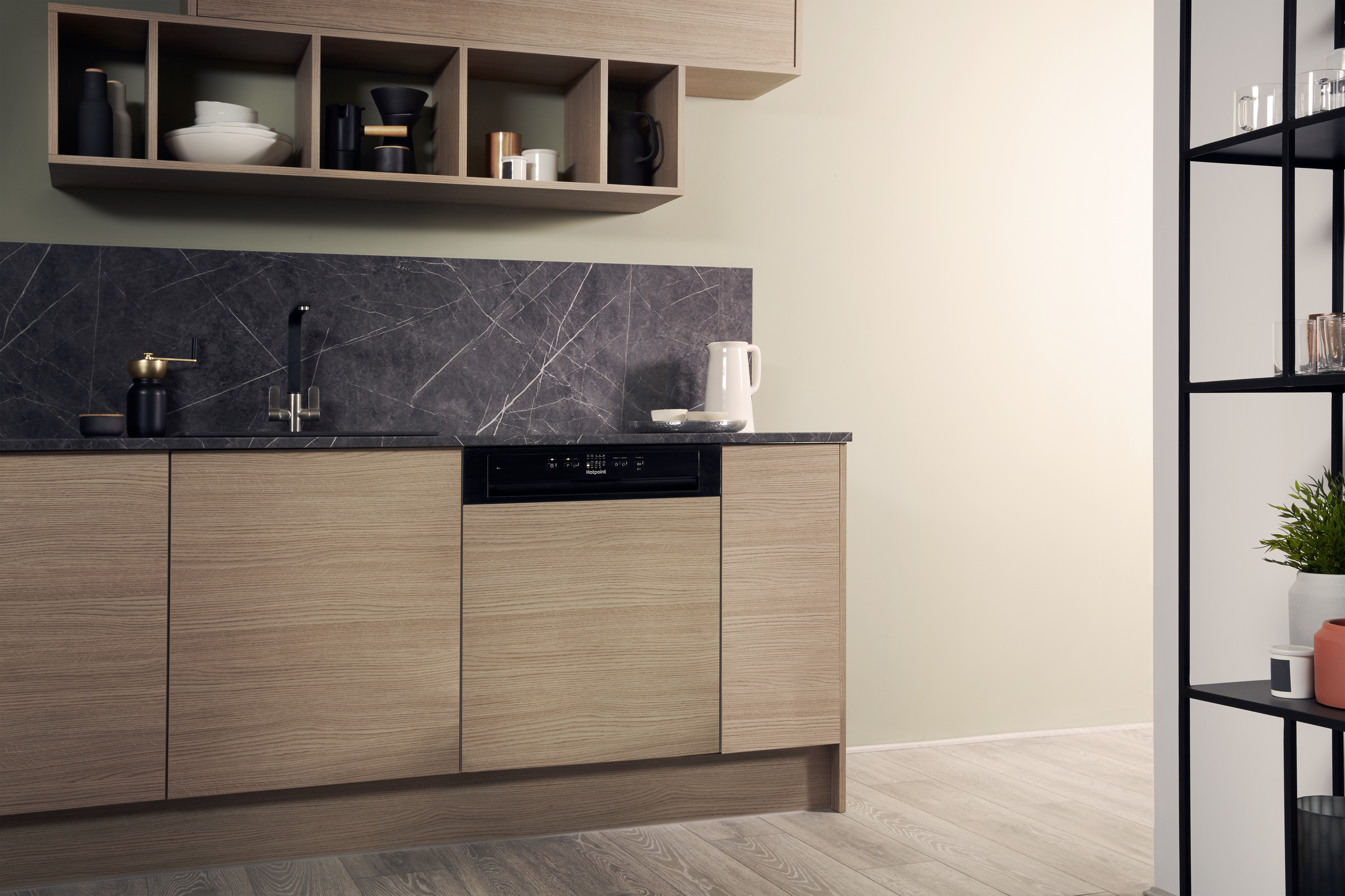Escena de cocina con gabinetes de madera clara, encimera oscura y lavavajillas empotrado. Pared beige.