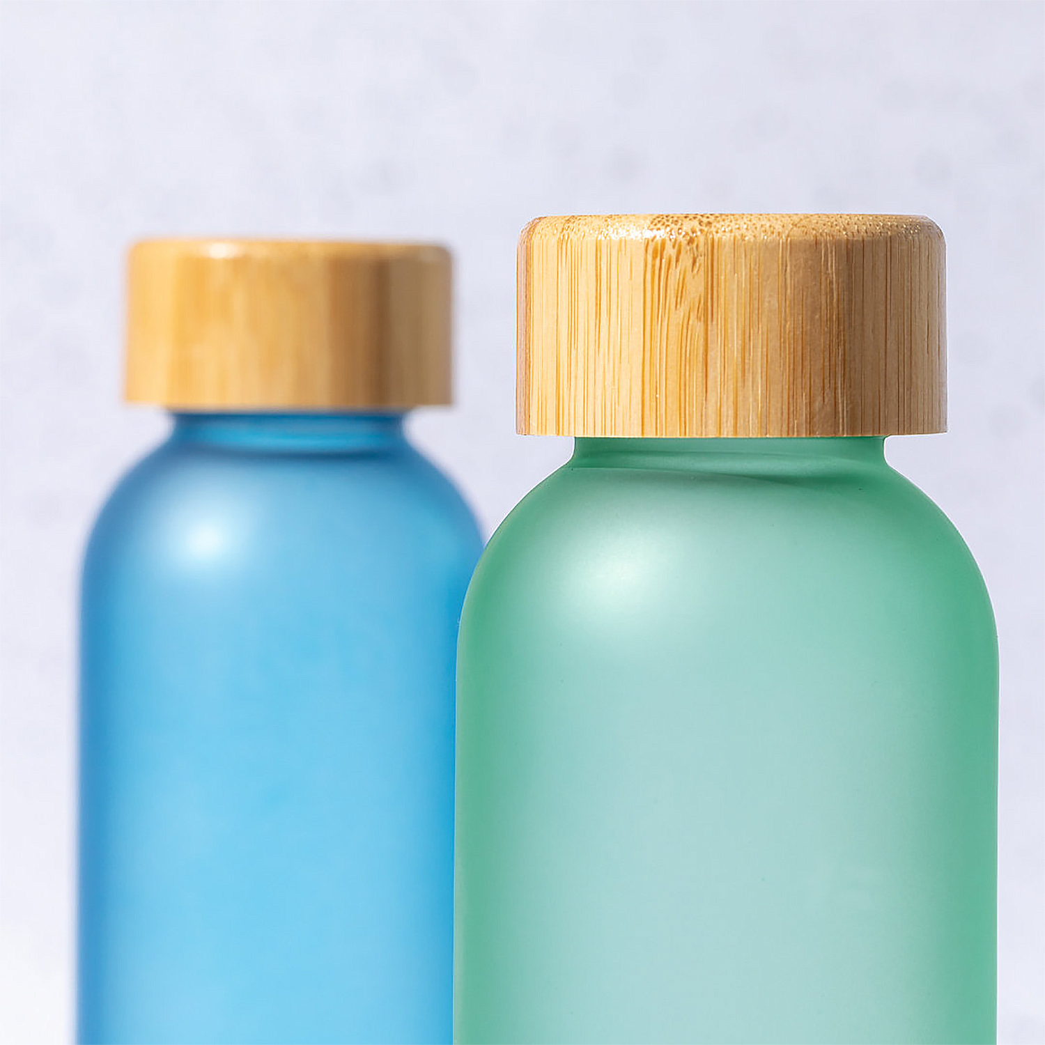Due bottiglie di vetro con coperchi di legno; una blu, una verde. Entrambe su sfondo bianco.