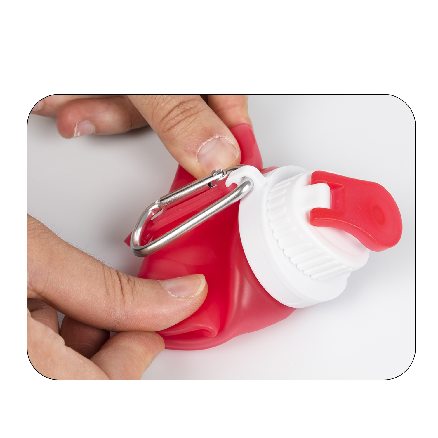 Manos sosteniendo una botella de agua roja plegable con una tapa blanca y un mosquetón plateado.