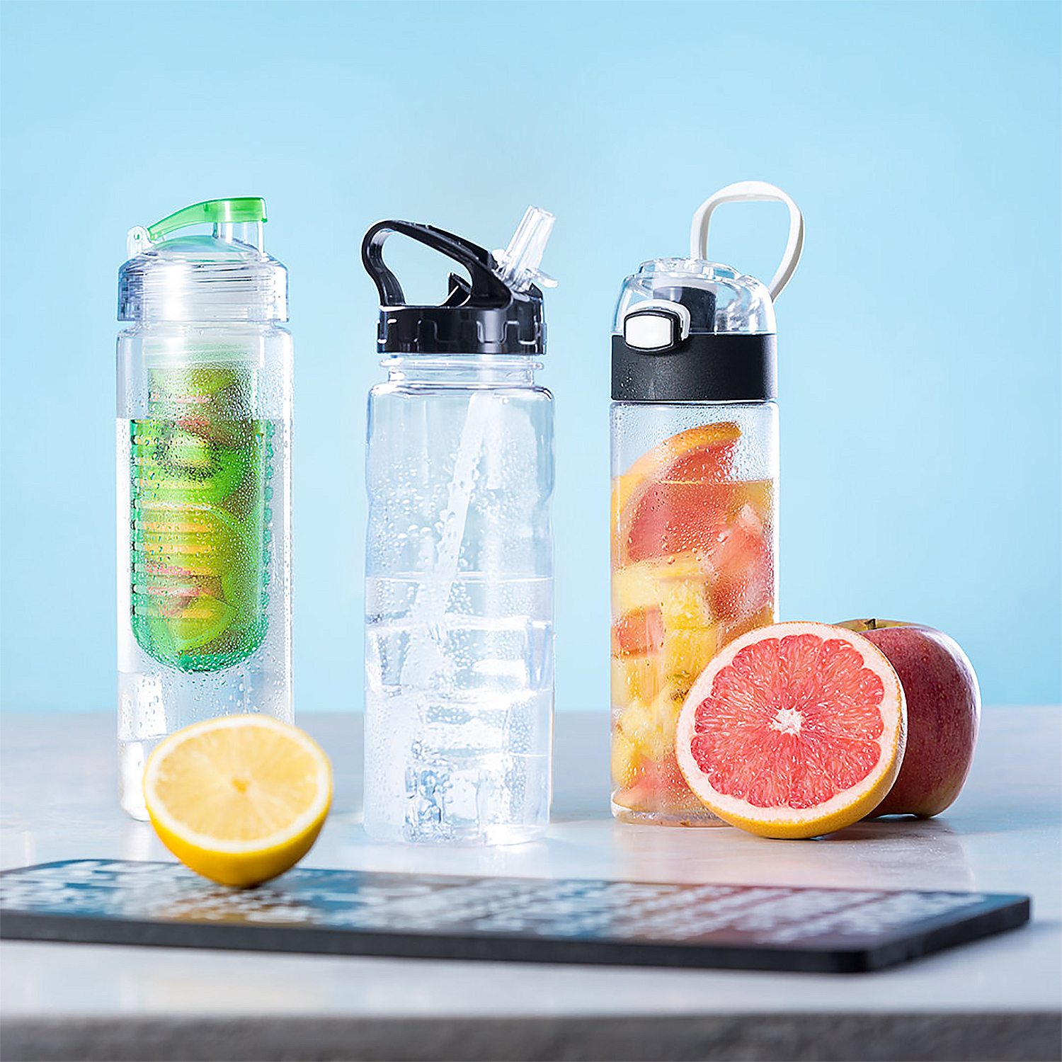 Tres botellas de agua con fruta y un limón. Fondo azul claro, y una mesa al frente.