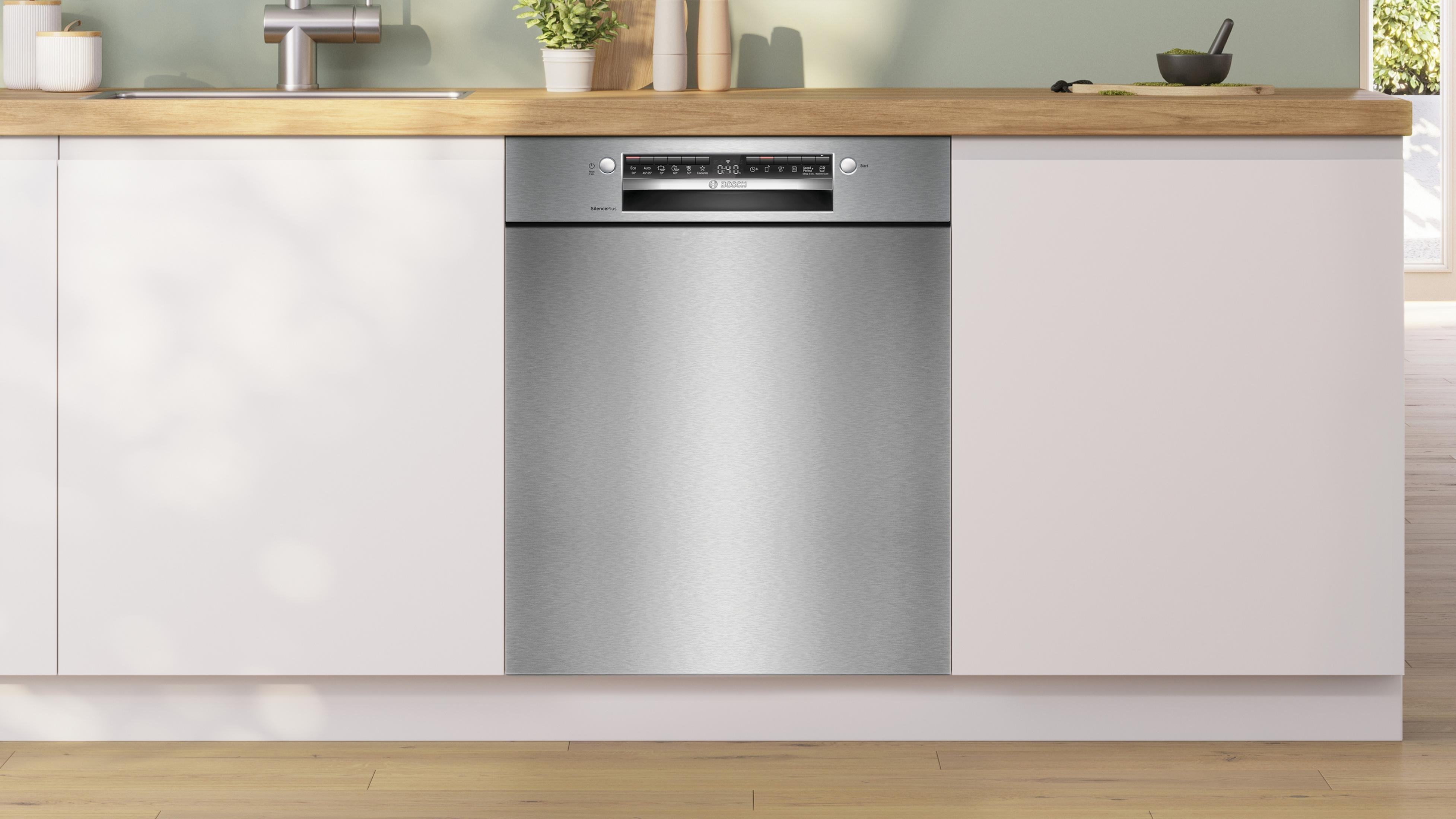 Una lavastoviglie in acciaio inossidabile integrata in un mobile da cucina bianco. La parte superiore è in legno.