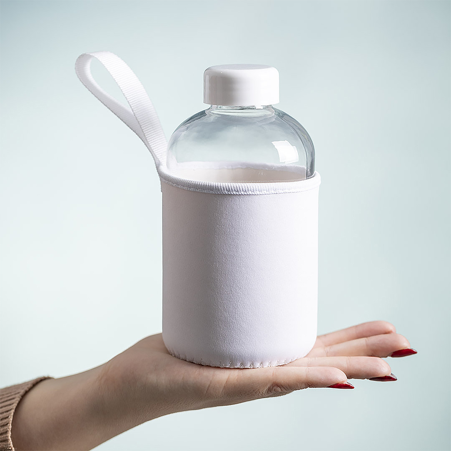 Una mano sosteniendo una botella de agua blanca en una funda blanca con tapa blanca, sobre fondo azul.