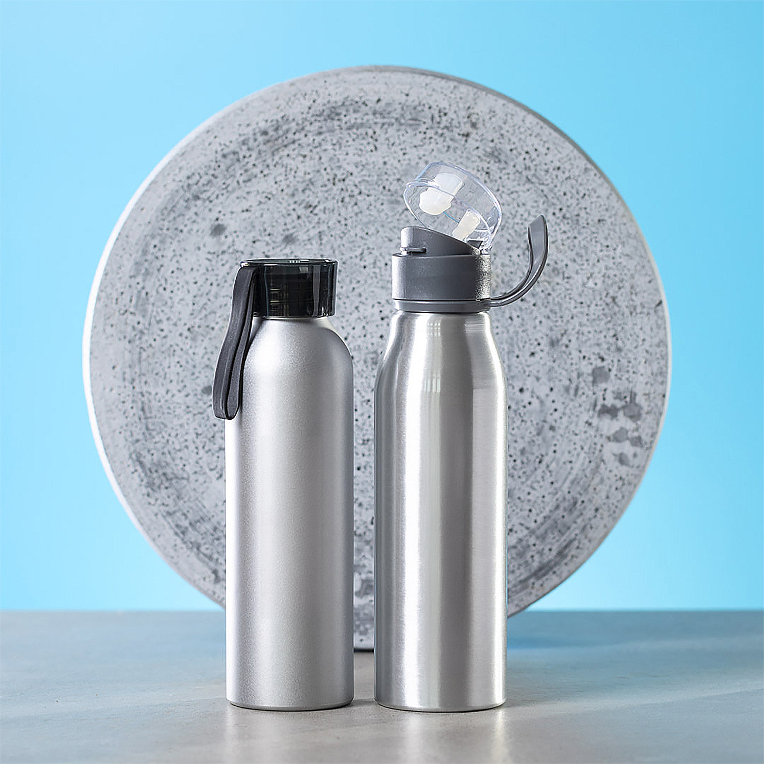 Dos botellas de agua plateadas contra un fondo azul. Una botella está abierta.