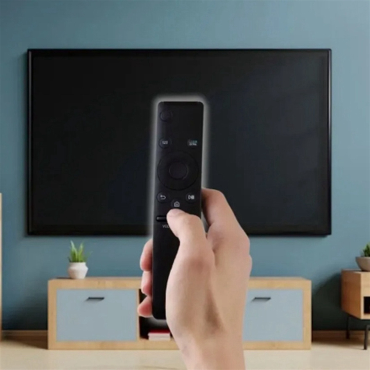 Hand hält TV-Fernbedienung auf einen Flachbildfernseher gerichtet.