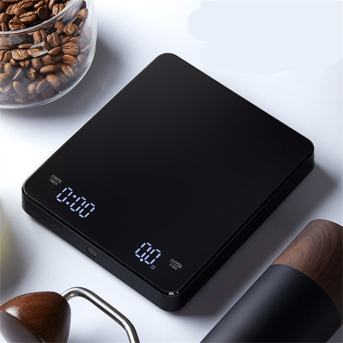 Schwarze digitale Küchenwaage mit Kaffeebohnenglas und Mühle im Hintergrund.