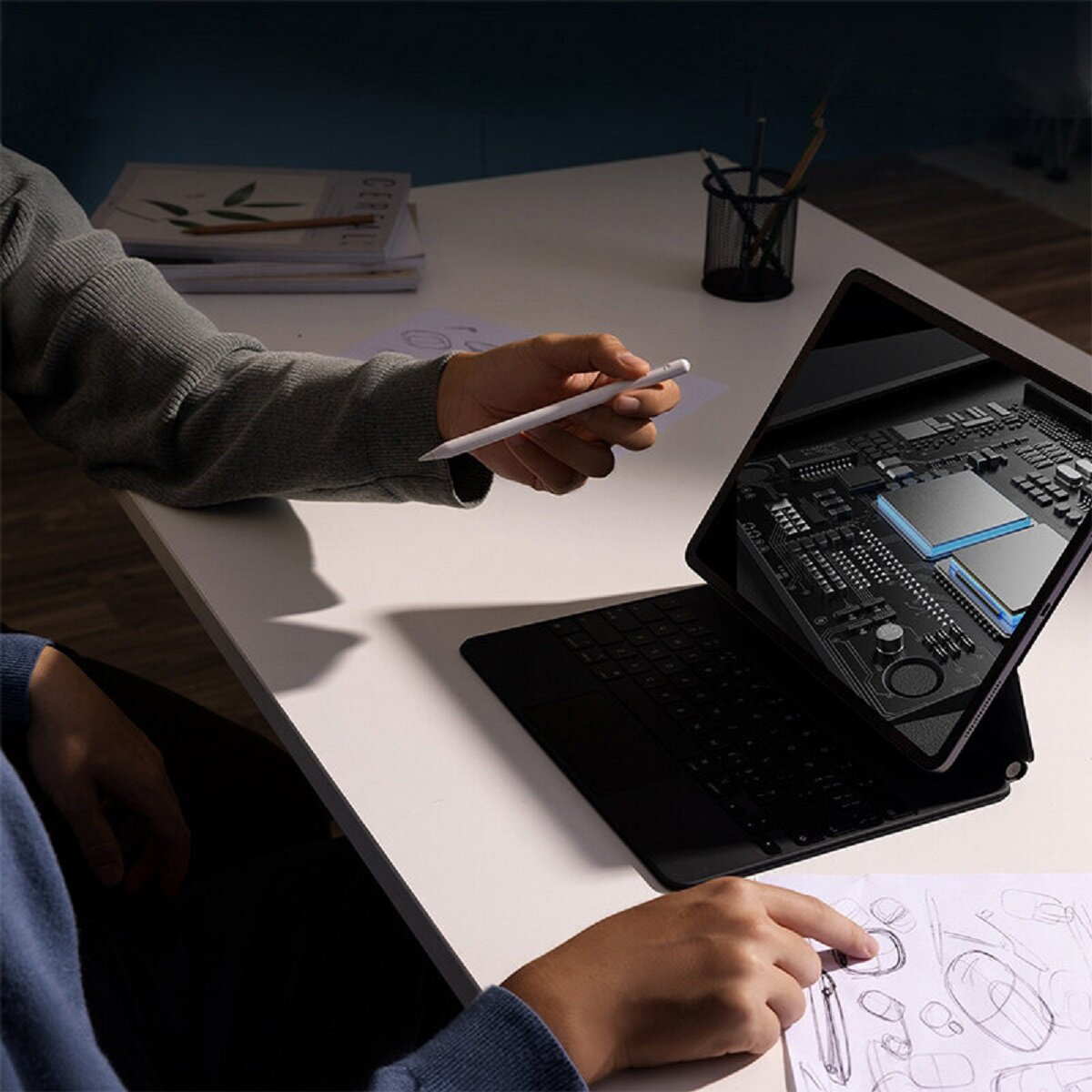 Osoba rysuje na papierze na stole. Otwarty jest tablet ze schematem systemu. Trzymany jest rysik.