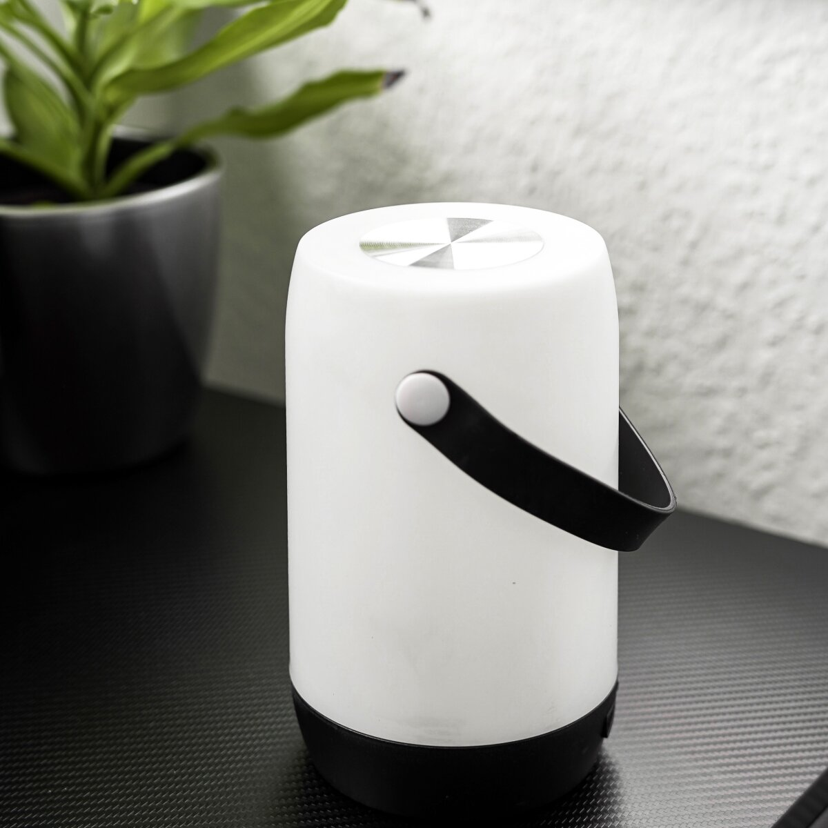 Zylindrische Tischleuchte in Weiß mit schwarzem Griff und Sockel.