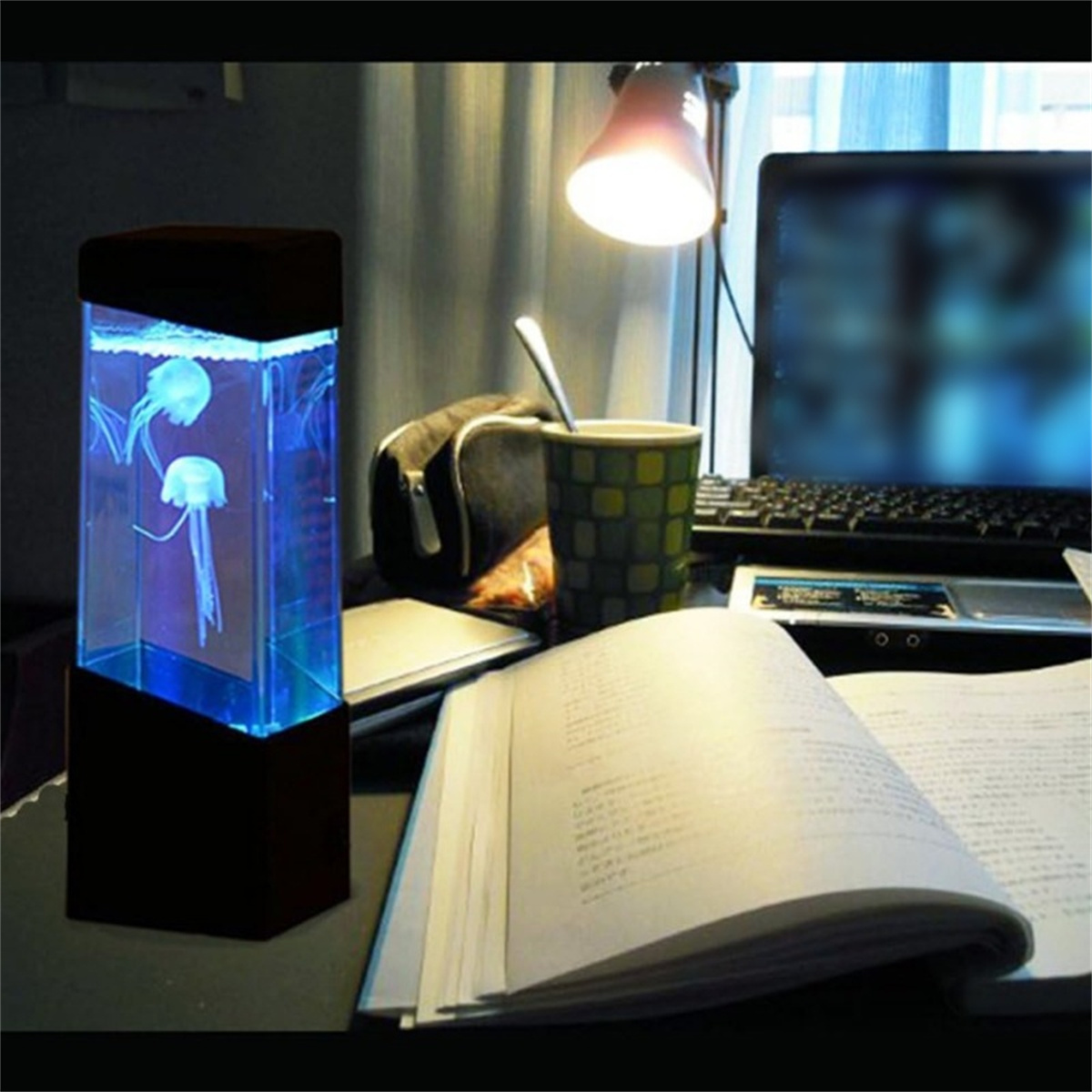 Quallenlampe mit zwei Quallen, einem Buch, einem Laptop und einer Tasse. Die Szene ist drinnen, gedämpfte Beleuchtung.