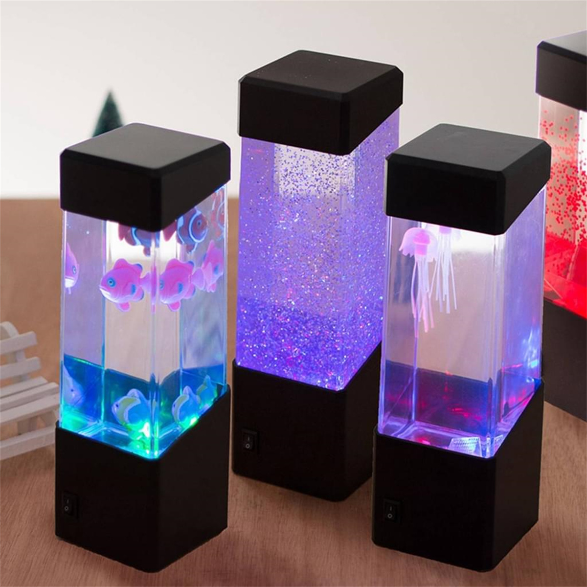 Drei quadratische Lampen mit schwarzen Basen. Eine hat Fische, die andere Glitzer, die dritte eine Qualle.