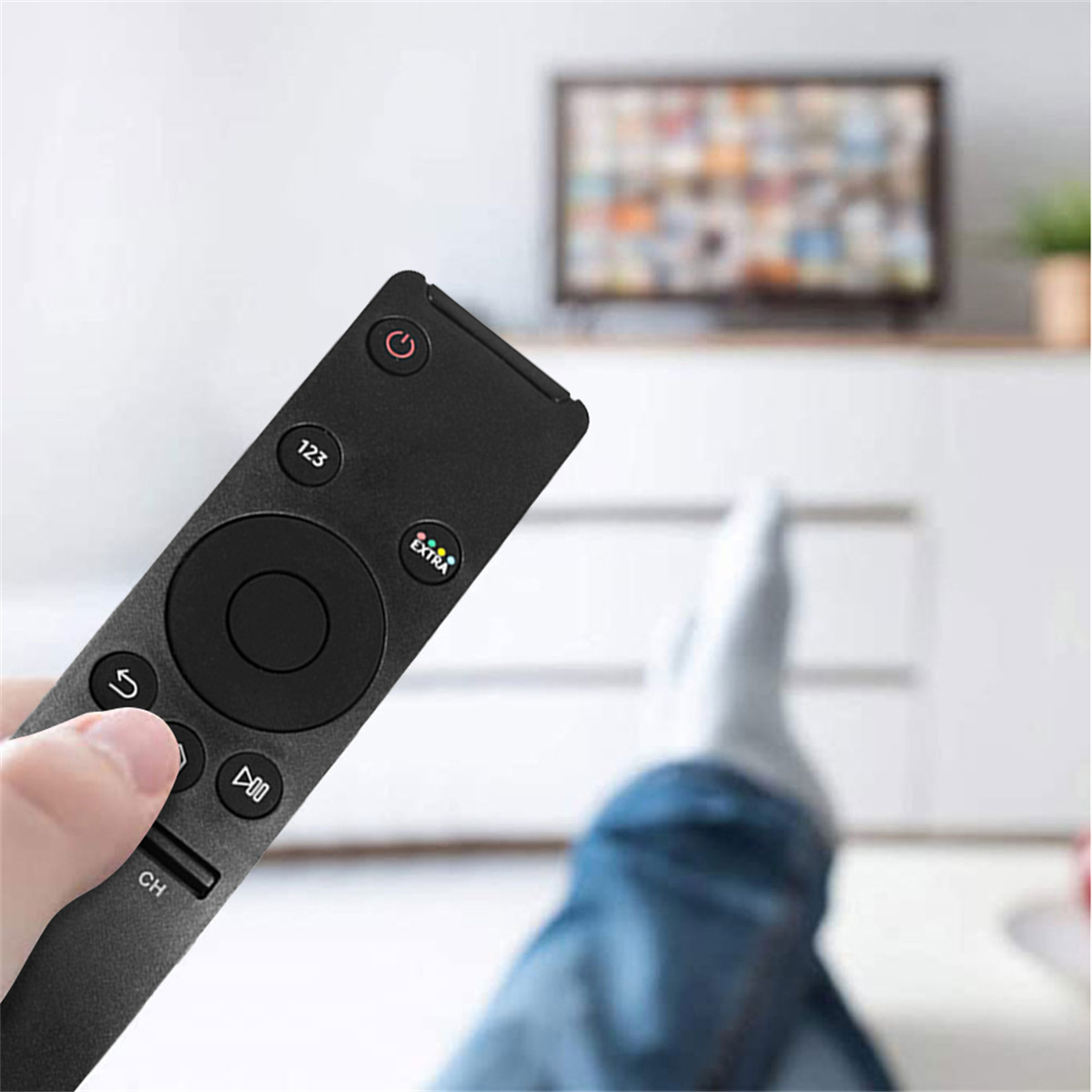Eine schwarze Fernbedienung in der Hand mit einem Fernseher im Hintergrund.