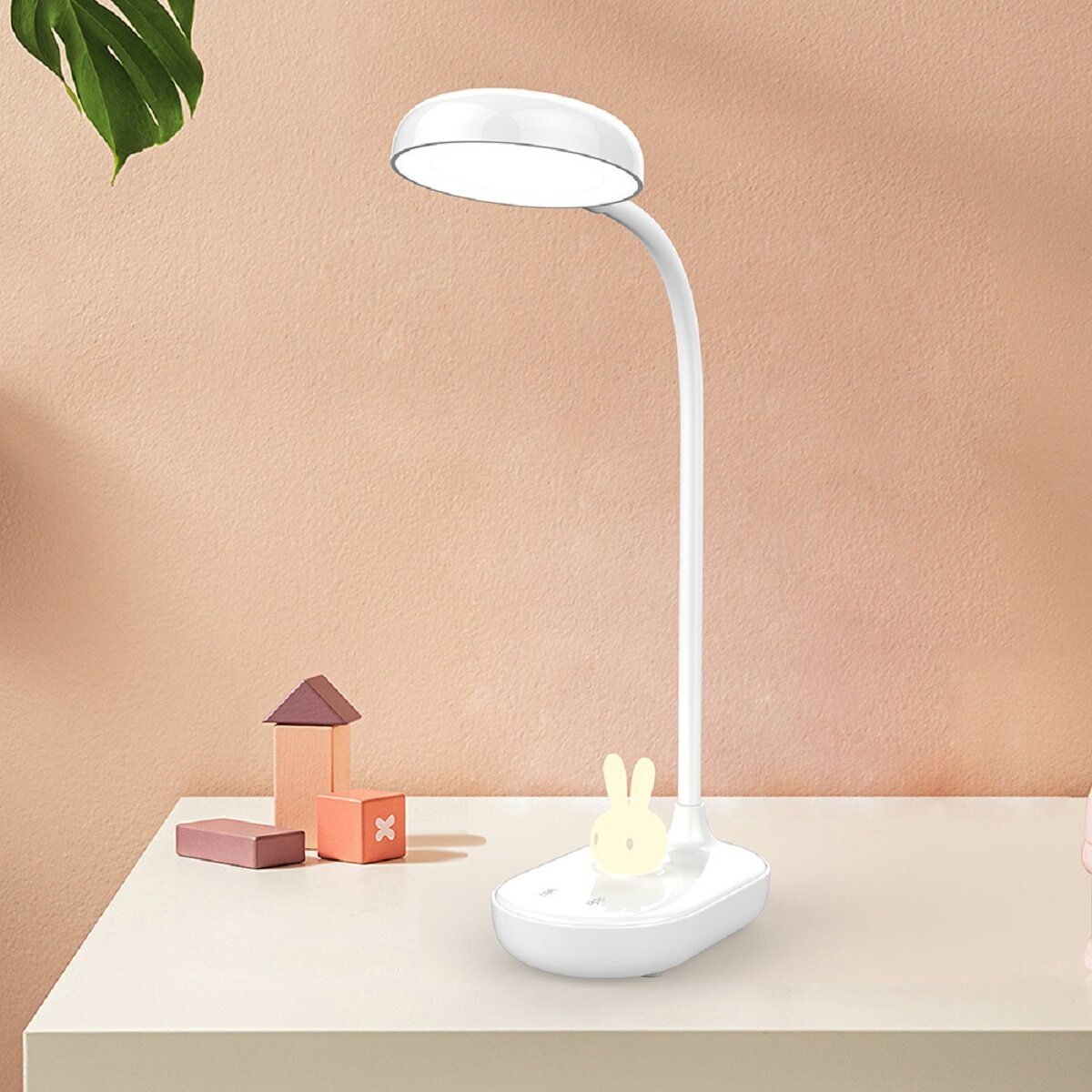 Weiße Schreibtischlampe mit Hasenfuß und Holzblöcken auf Pfirsichhintergrund.