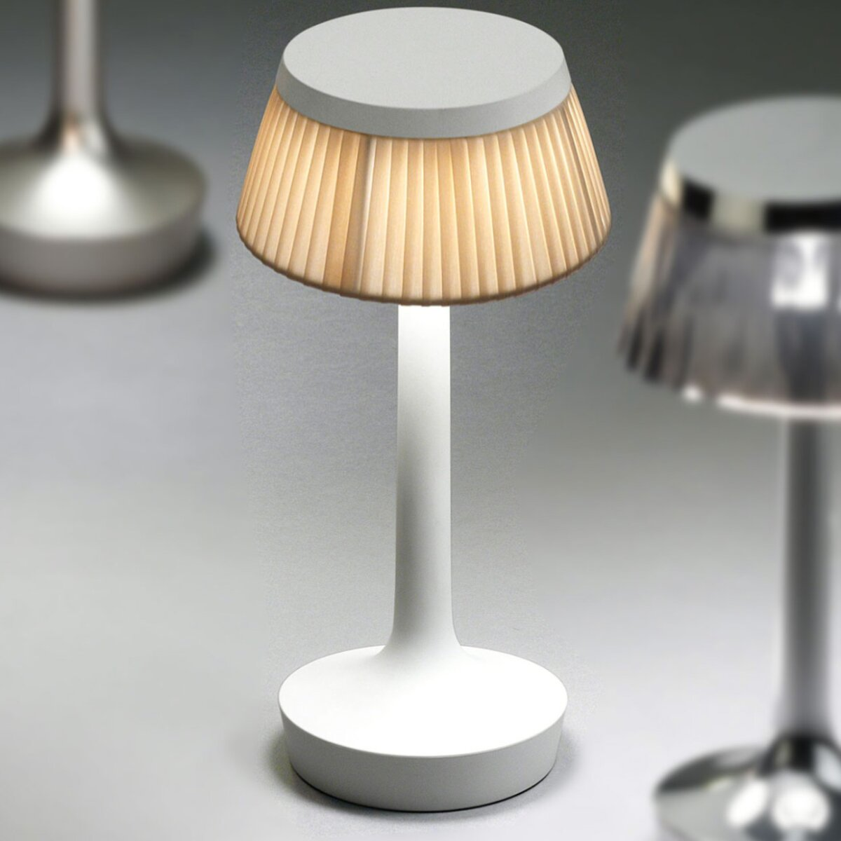 Eine weiße Tischlampe mit einem plissierten Lampenschirm. Im Hintergrund sind weitere Lampen zu sehen.