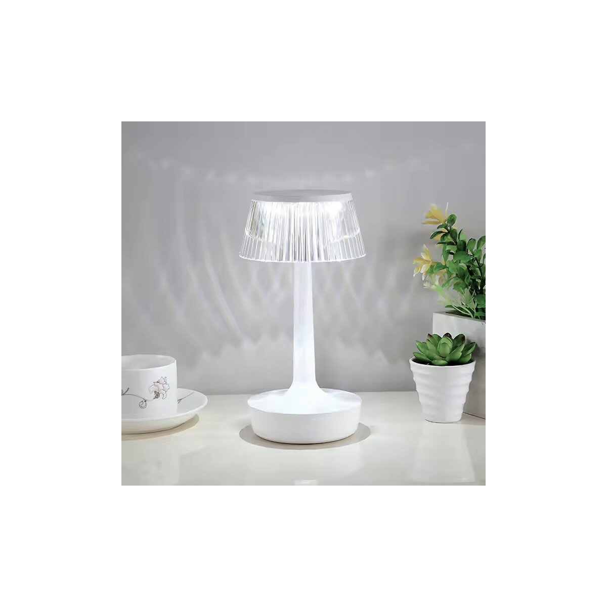 Eine weiße Tischlampe mit weißem Sockel und durchscheinendem Lampenschirm, neben einer Tasse und Pflanze.
