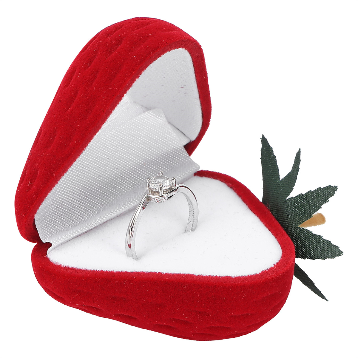 Ein Ring in einer roten, herzförmigen Schachtel mit weißem Satin-Innenraum und einer grünen Blume daneben.