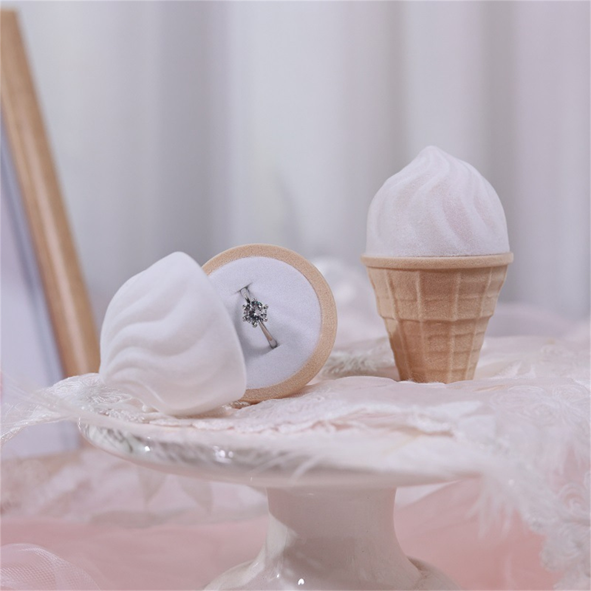 Ring in einer samtigen, eiscreme-förmigen Schachtel. Die Schachtel steht auf einer Tortenplatte.