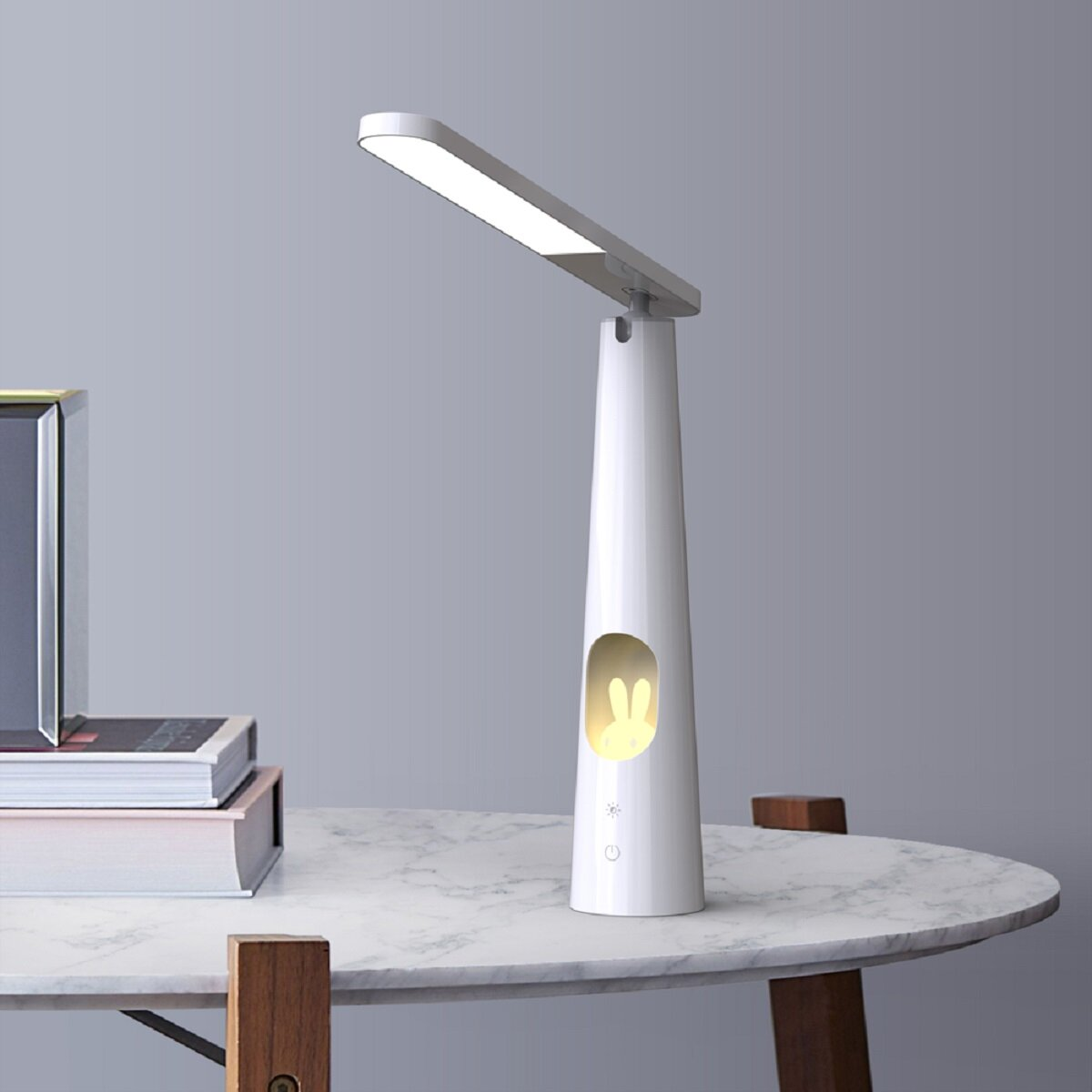 Weiße Schreibtischlampe mit Hasenlicht. Die Lampe steht auf einem Tisch. Ein Buch und ein Bilderrahmen sind darauf.