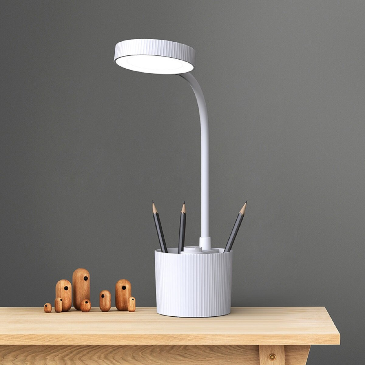 Weiße Schreibtischlampe mit Stifthalter. Holzdekor links, Stifte im Halter.