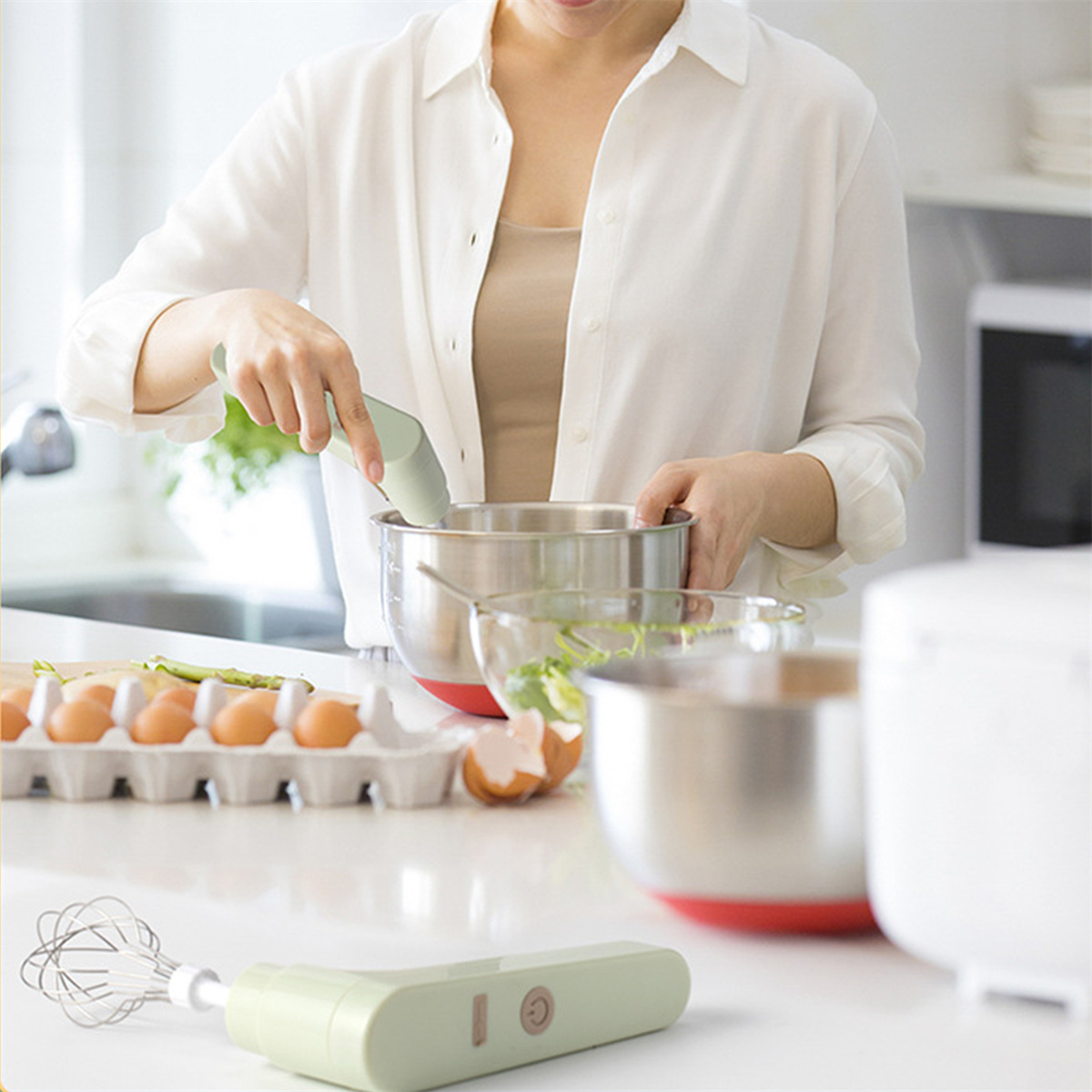 Frau, die einen Handmixer benutzt, um Zutaten in einer silbernen Schüssel zu verrühren. Eier in einem Karton im Hintergrund.