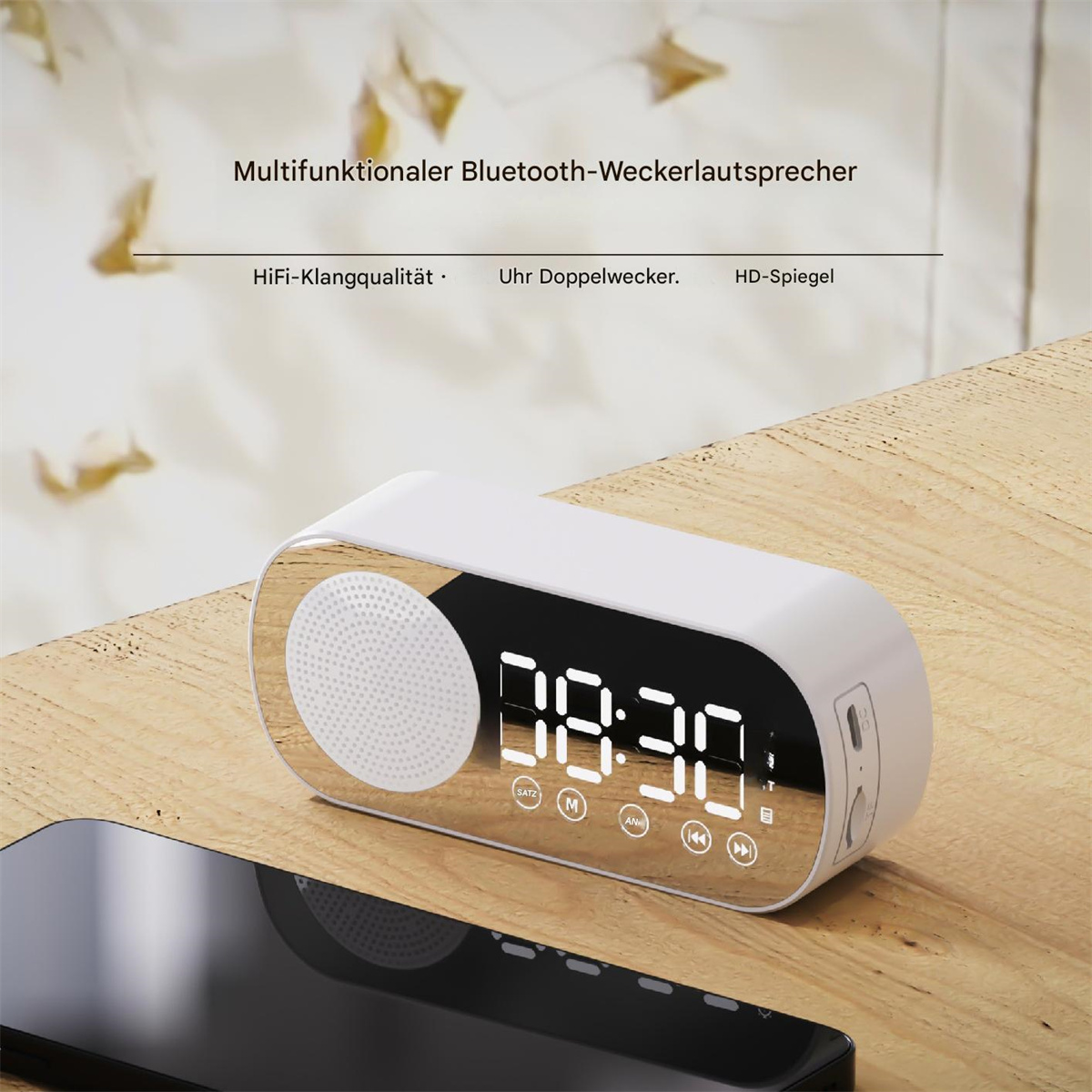 Ein weißer Bluetooth-Lautsprecher mit digitaler Uhranzeige. Auf einem Holztisch mit einem schwarzen Telefon.