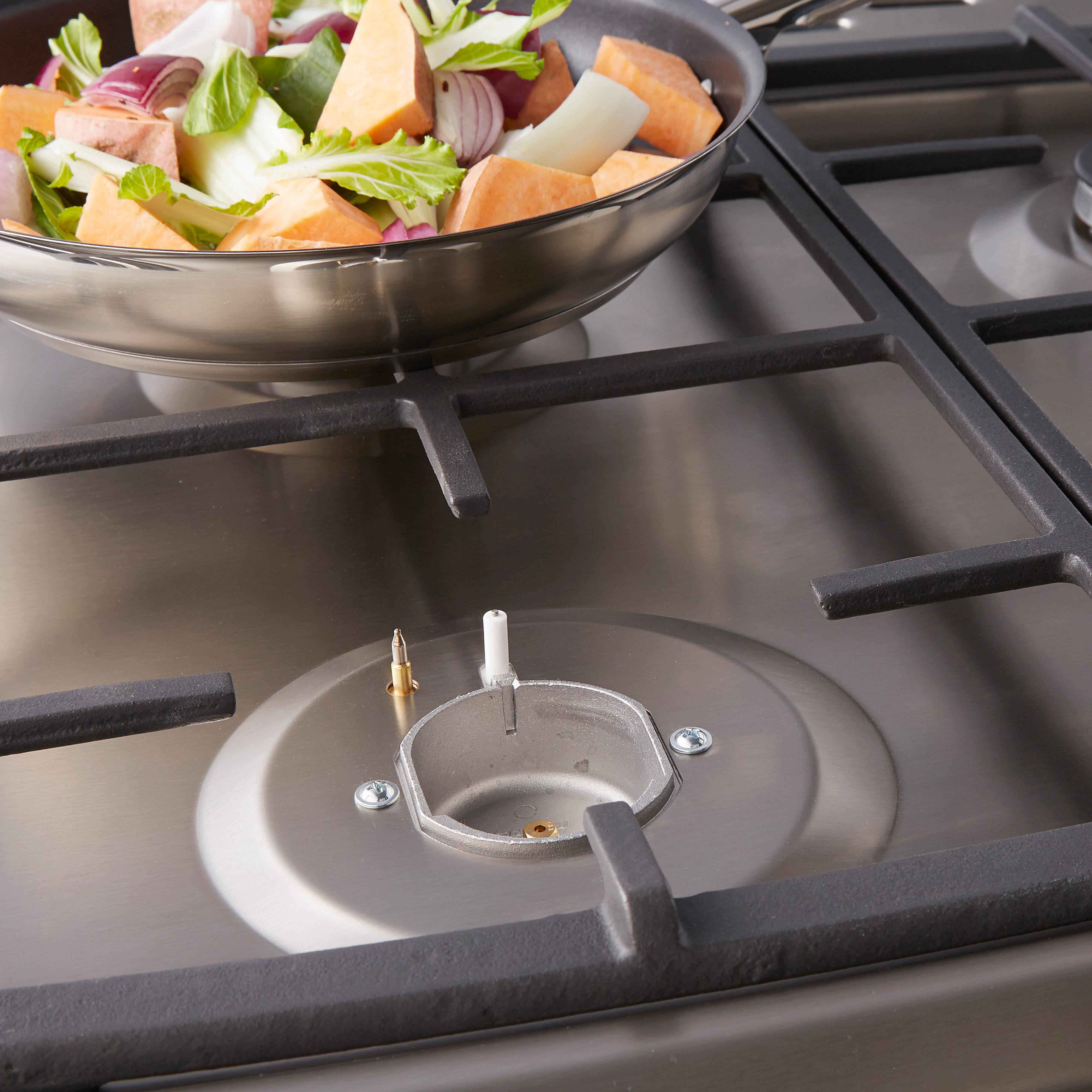Een roestvrijstalen kookplaat met een pan met gesneden groenten, klaar om te koken. Zwarte kookplaatdetails.