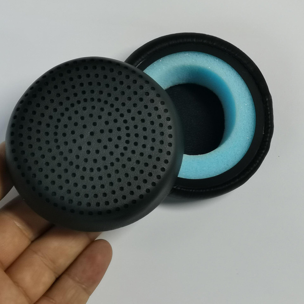 Zwei schwarze Kopfhörerpolster, eines mit Löchern, das andere mit blauem Schaumstoff.