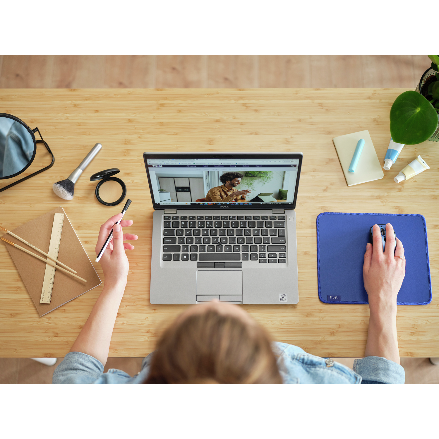 Widok z góry na miejsce pracy. Laptop, mysz, notatnik, akcesoria i ręce osoby.