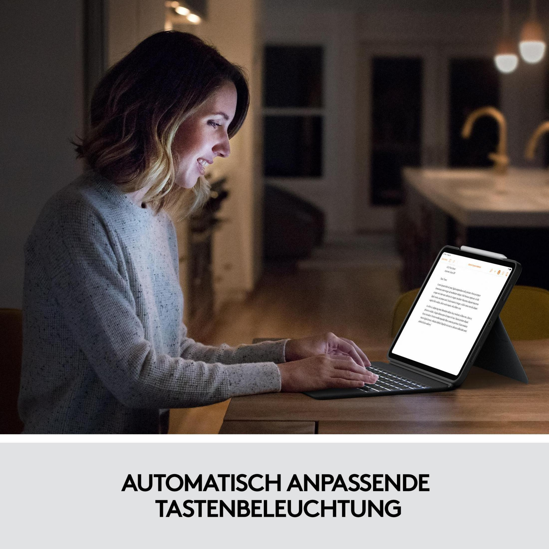 Kobieta pracuje na tablecie z klawiaturą w słabo oświetlonym pokoju, ze stołem i dwoma światłami.