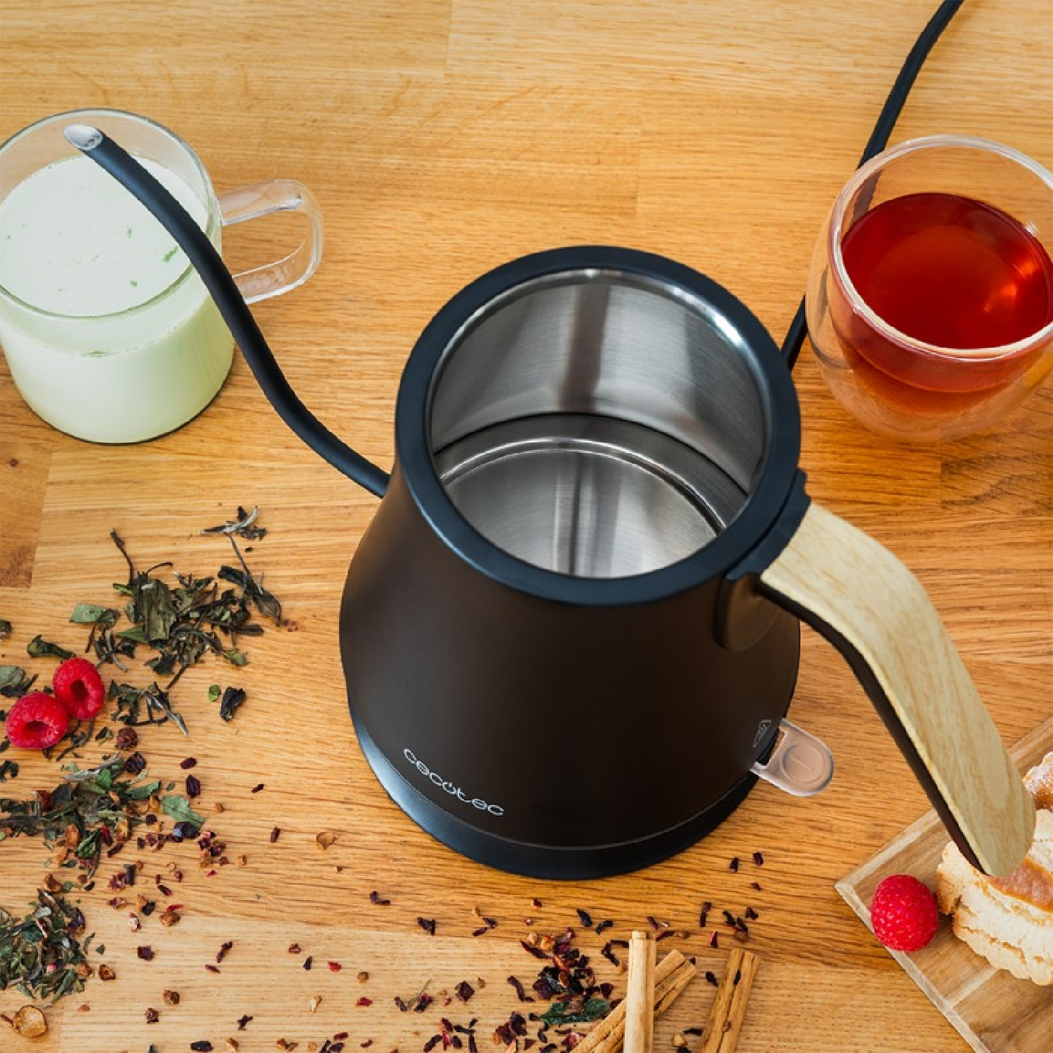 Schwarzer Wasserkocher, zwei Glasbecher, Teeblätter und Beeren auf einem Holztisch.