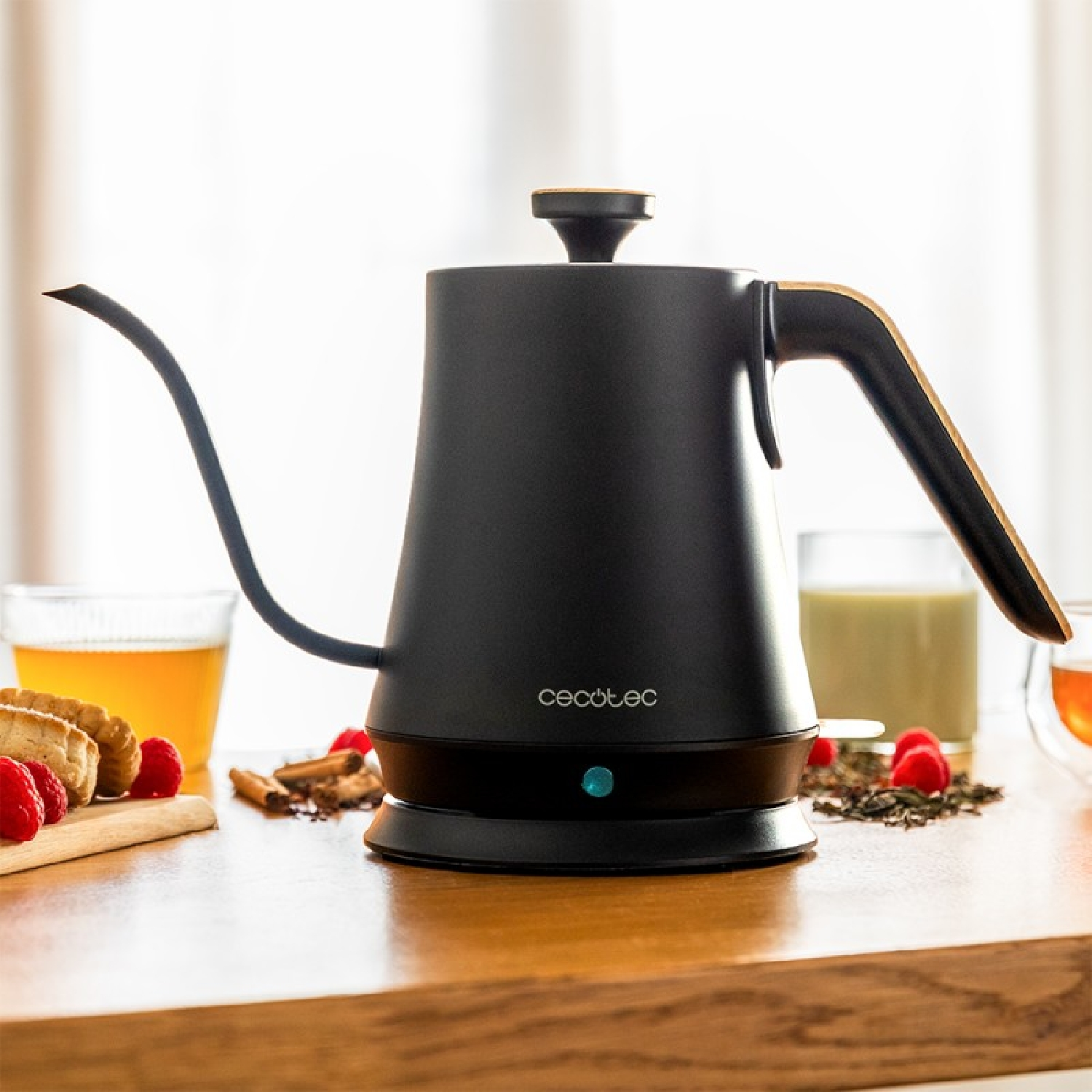 Schwarzer elektrischer Wasserkocher mit langem Ausguss, neben Himbeeren, Keksen und anderen Gegenständen auf einem Holzbrett.
