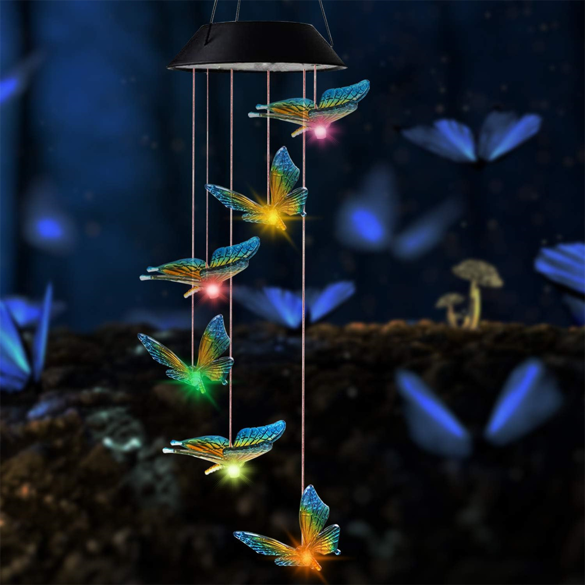 Schmetterlings-Windspiele hängen draußen. Die Schmetterlinge sind in verschiedenen Farben beleuchtet. Dunkelblauer Hintergrund.
