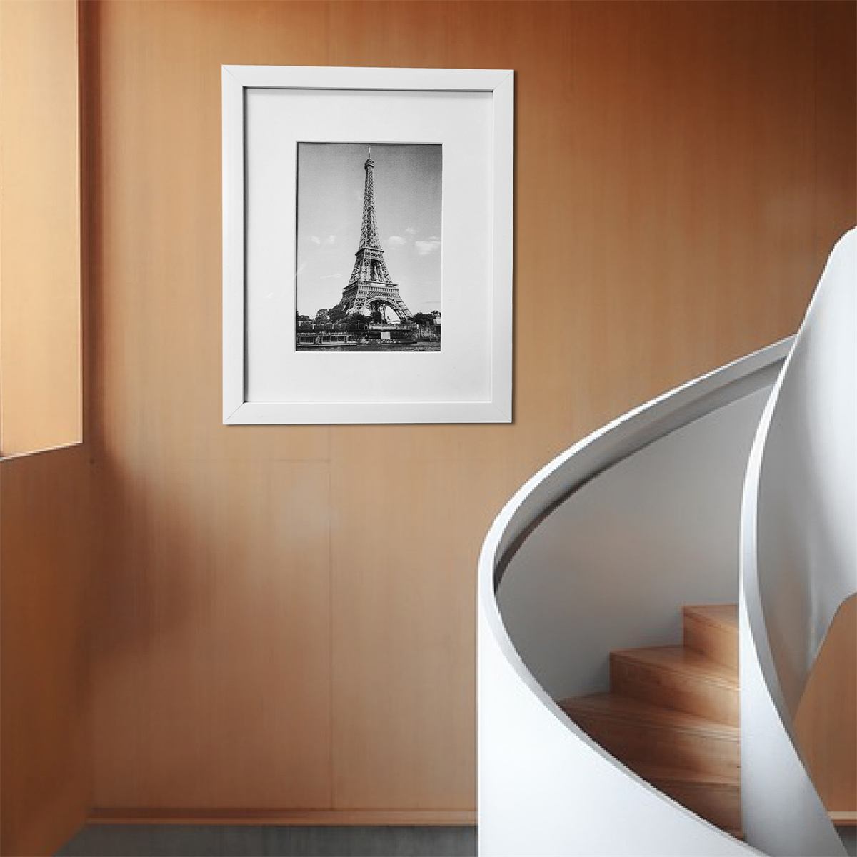 Schwarz-Weiß-Foto des Eiffelturms in weißem Rahmen an beiger Wand, mit Wendeltreppe.