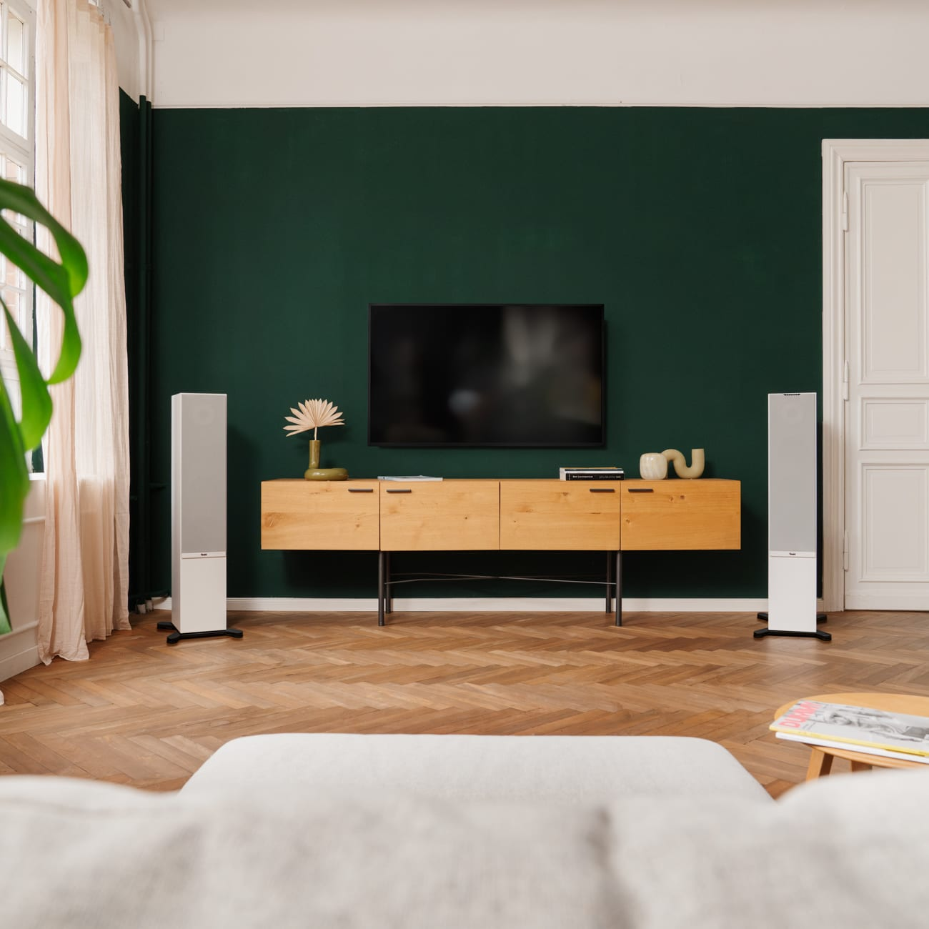 Een woonkamer met een tv, luidsprekers, een houten kast en een groene muur.