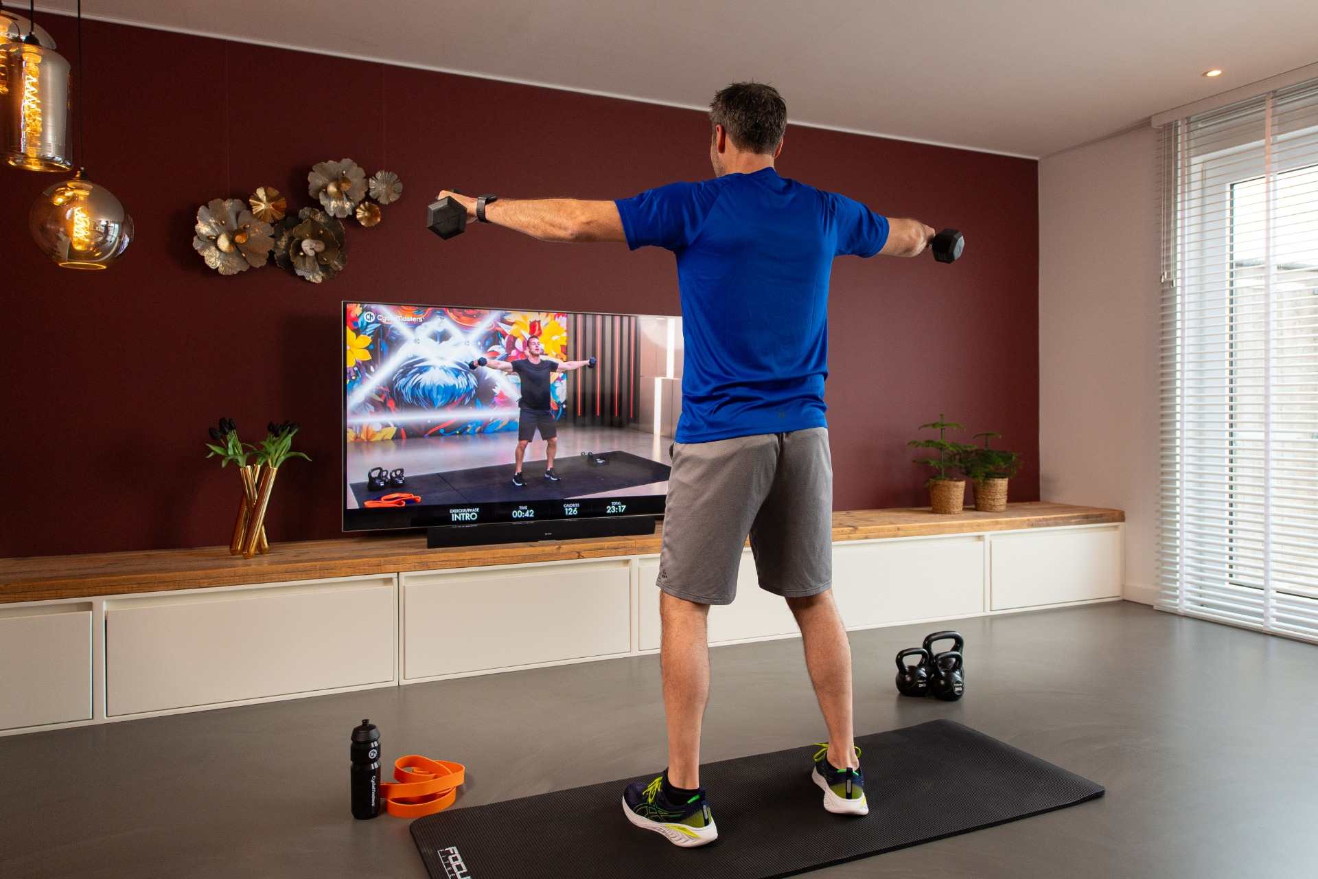 Homme en chemise bleue faisant des exercices avec des haltères devant la télé.