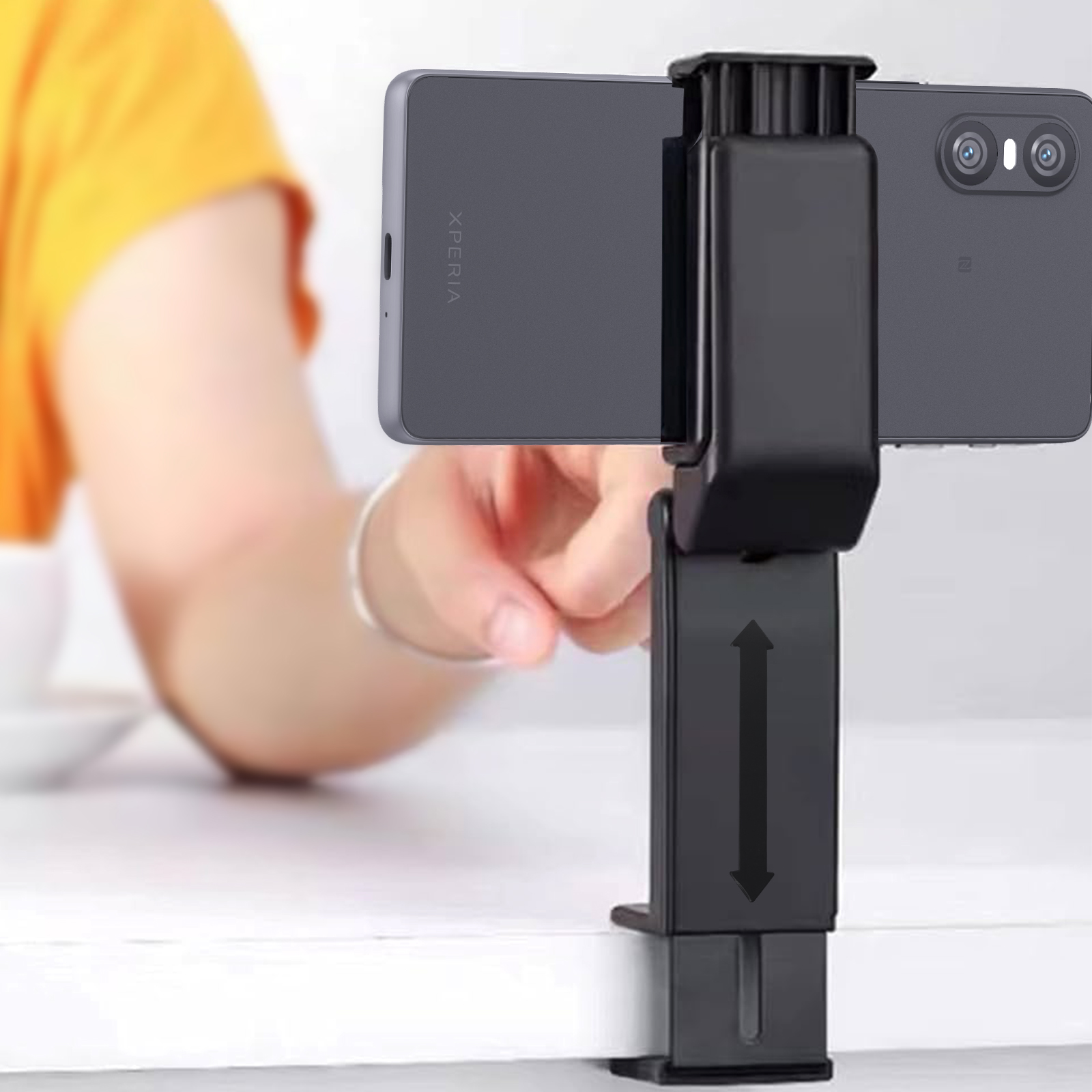 Un téléphone tenu par une personne, fixé à un support noir. Le support peut être ajusté de haut en bas.