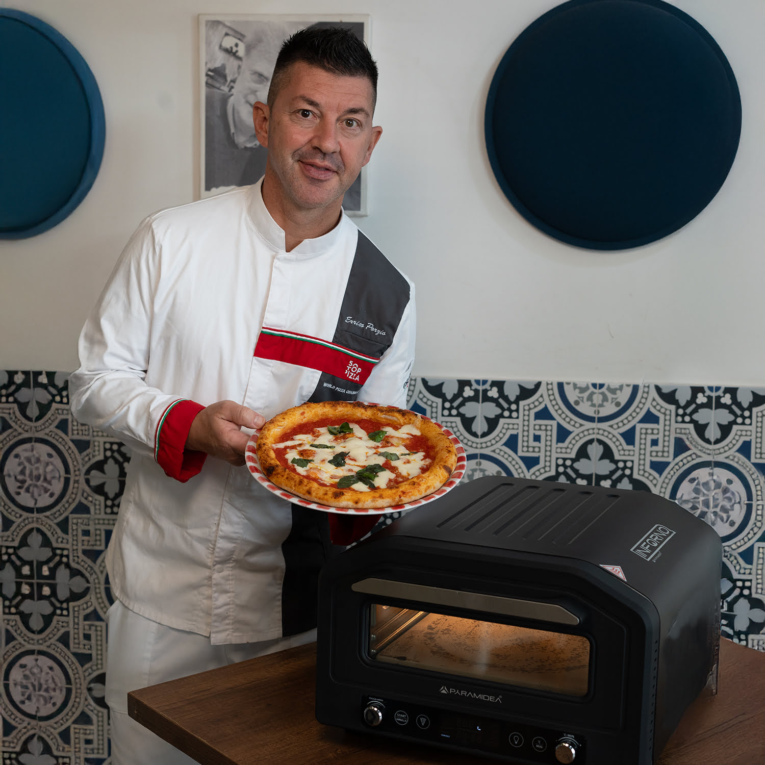 Uomo che tiene in mano una pizza vicino a un forno per pizza.