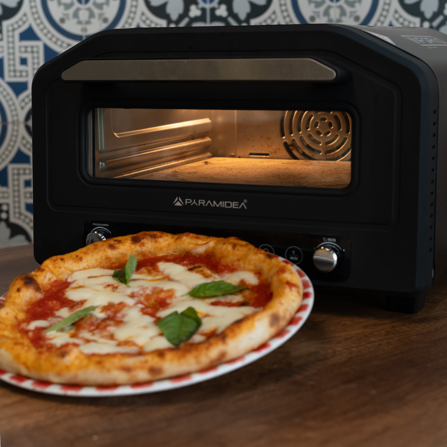 Un mini forno Paramidea nero con una pizza all'interno, su un tavolo di legno.