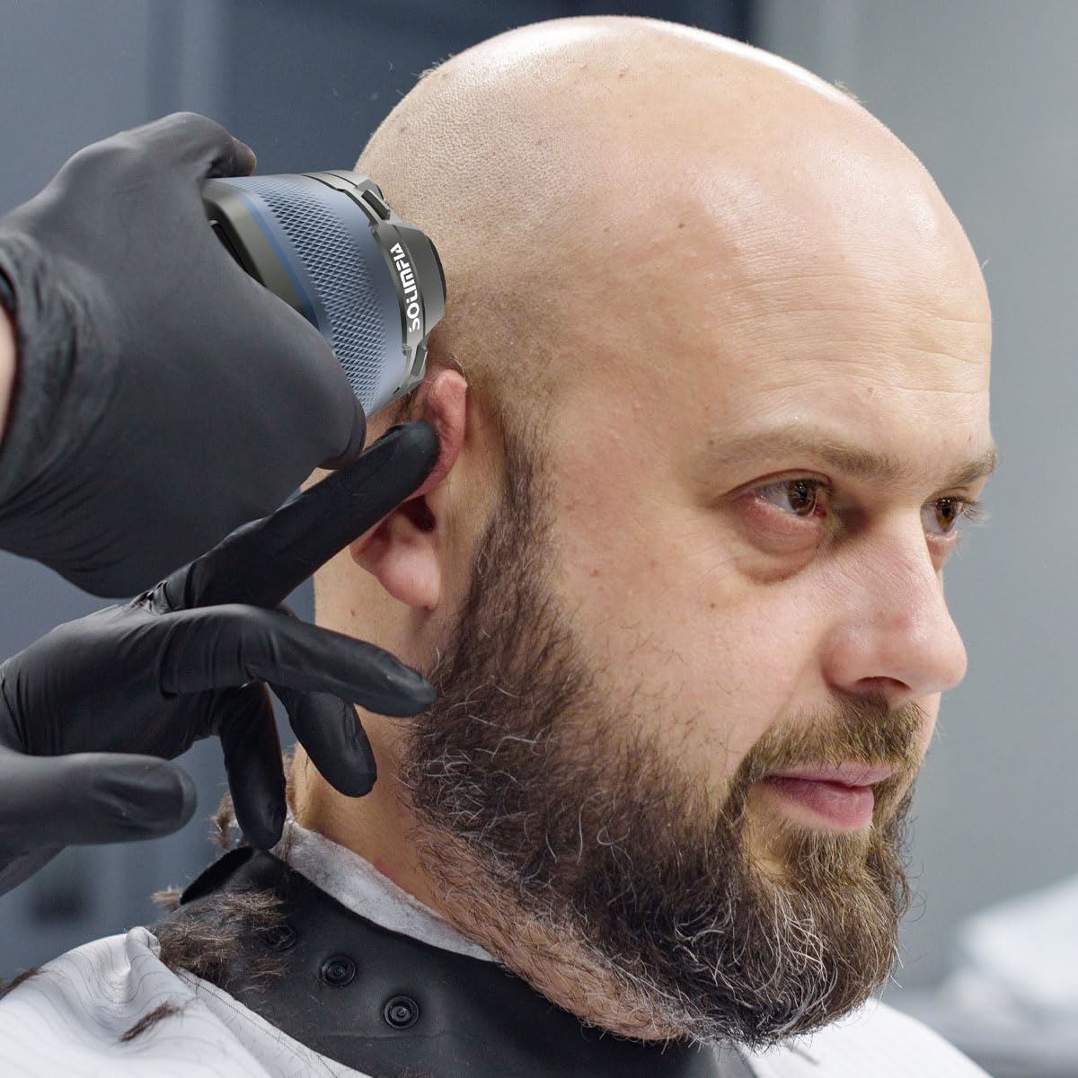 Der Kopf einer Person wird mit einem Trimmer rasiert. Die Person hat einen Bart und der Trimmer ist blau und grau.