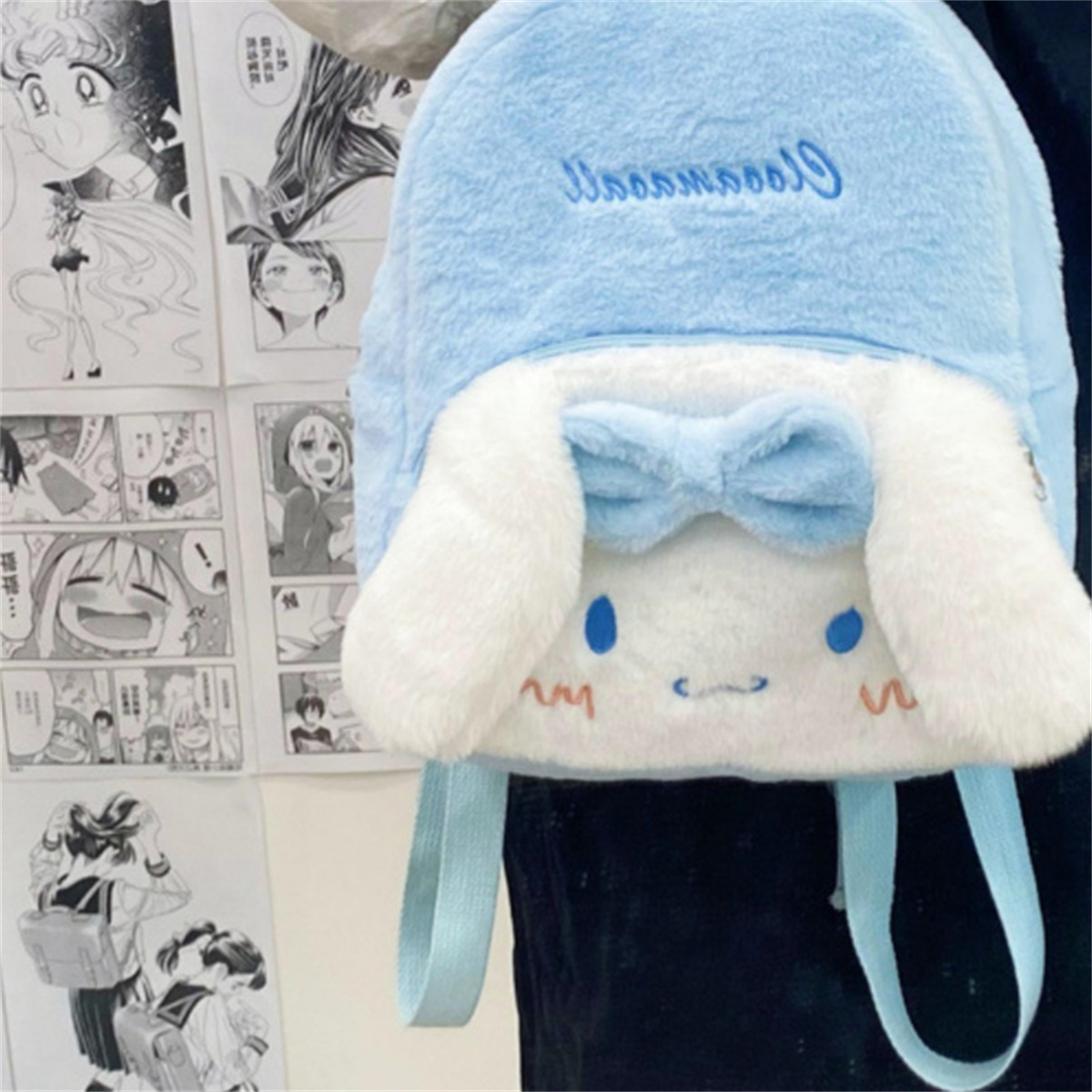 Ein hellblauer Cinnamoroll-Rucksack mit weißen Ohren und einer blauen Schleife, vor einem Hintergrund von Manga-Seiten.