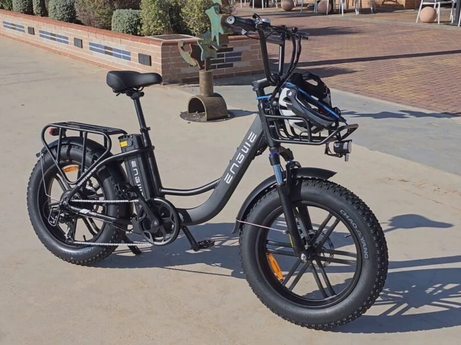 Bicicletta elettrica nera parcheggiata su un'area pavimentata vicino a un muro con un casco.